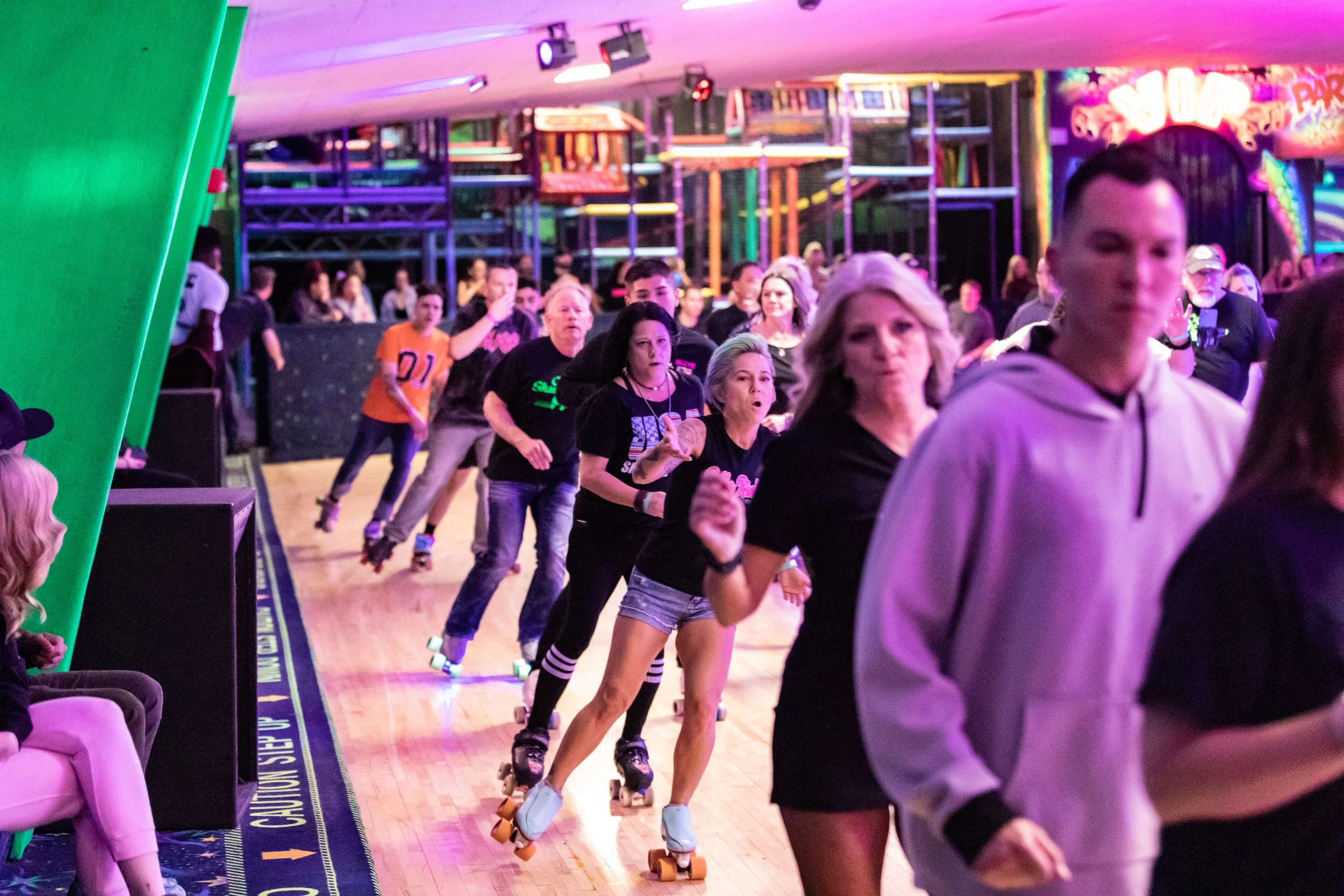 People roller skating in an indoor skate rink with colorful neon lights and structures in the background.