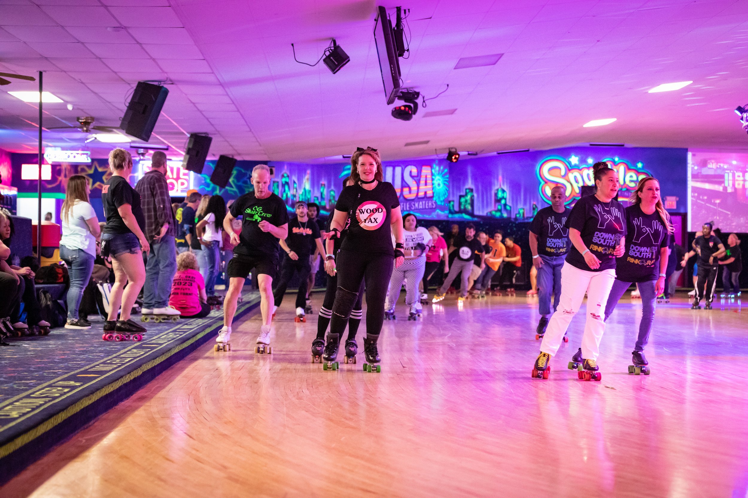 People roller skating on a rink with colorful neon signs and club lighting, including a 'USA' sign and a 'Spare' sign in the background.