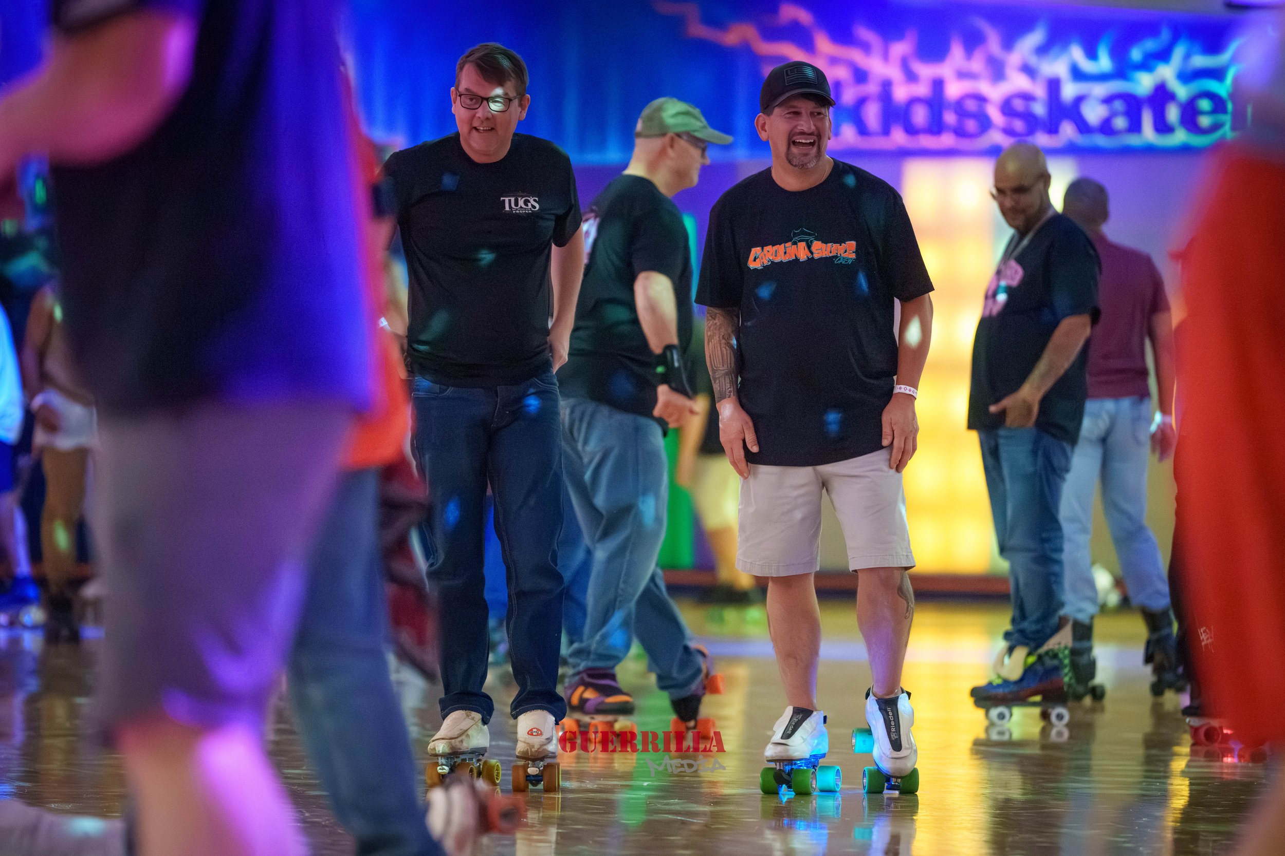 People roller skating in an indoor rink with colorful lights and a 'kids skate' sign in the background.