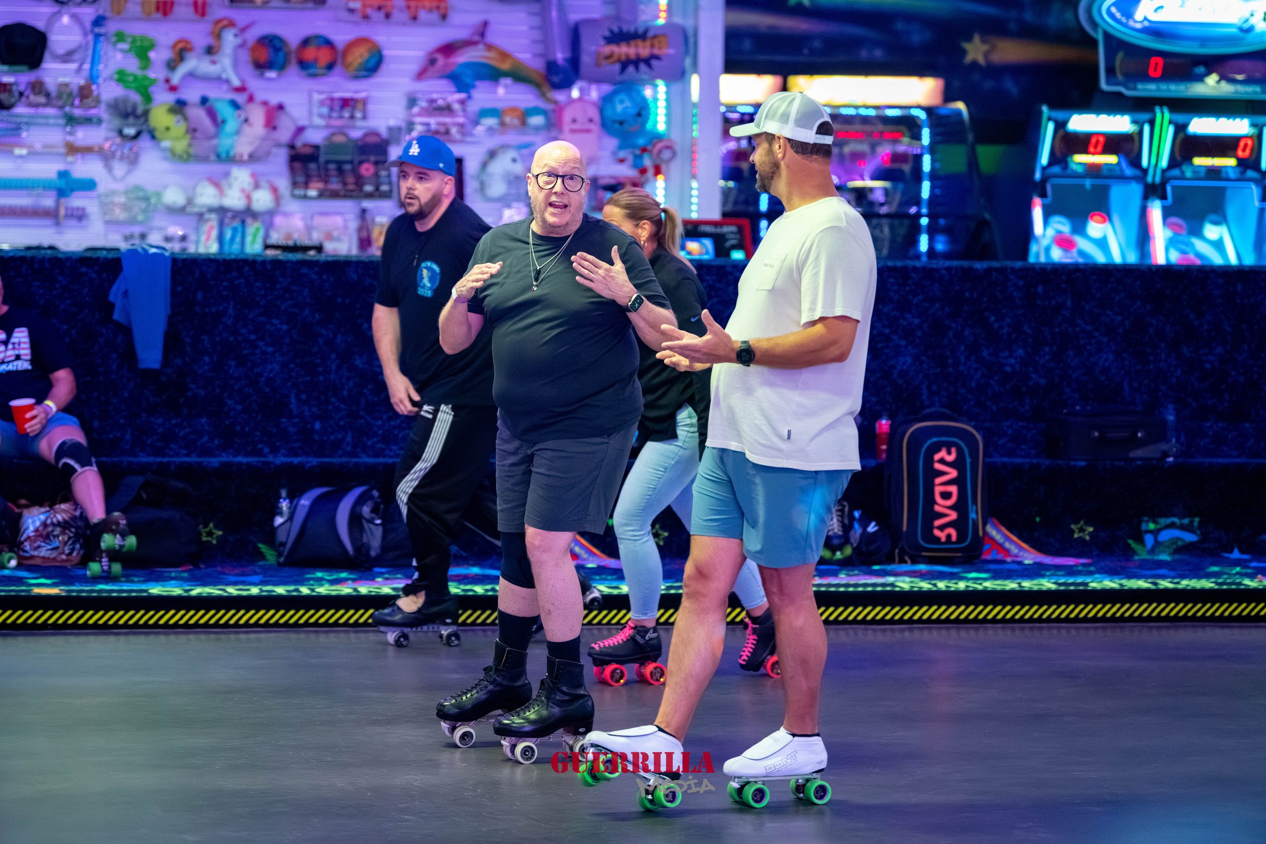 People roller skating in an indoor skating rink with neon lights, arcade games, and colorful decorations in the background.