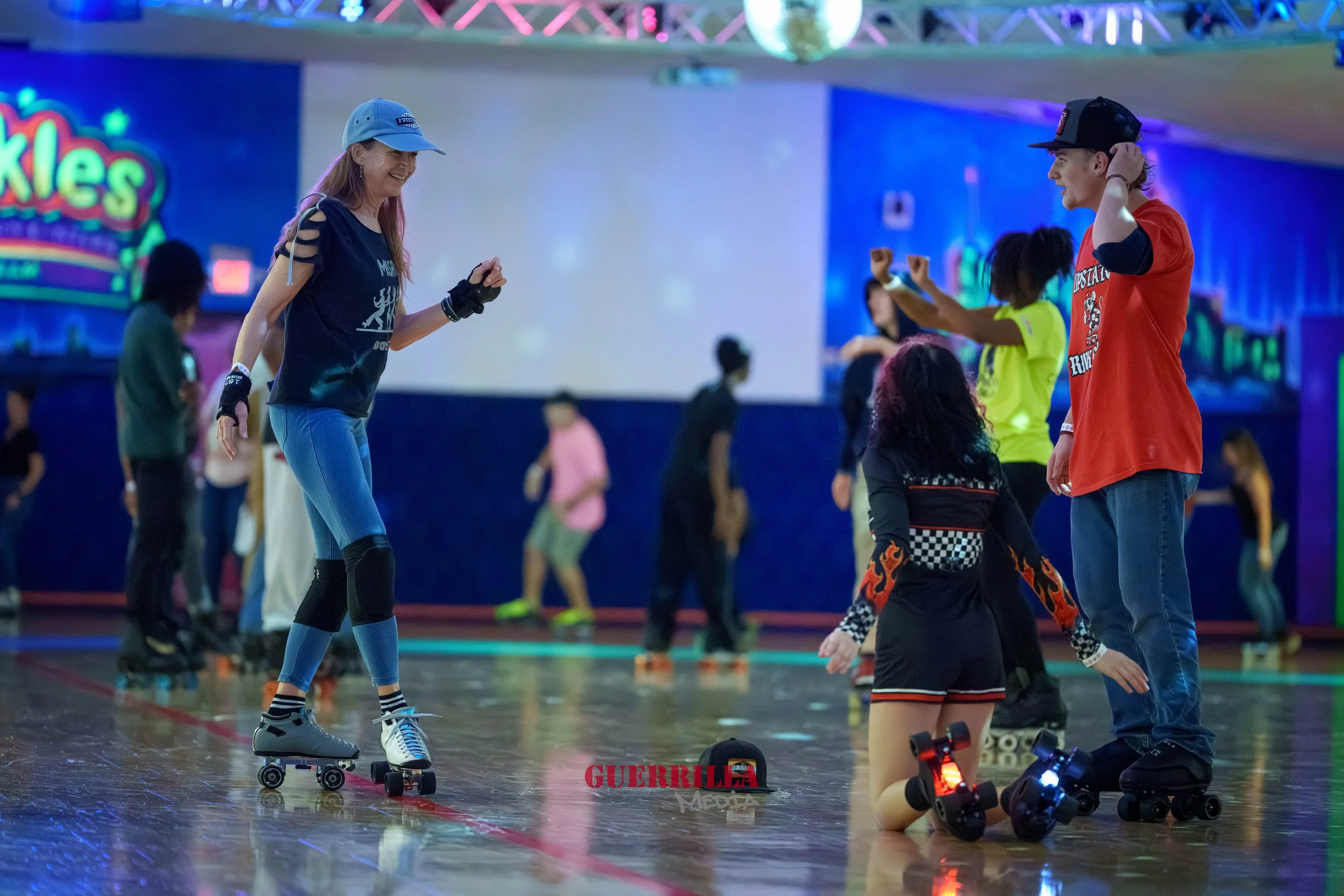 People roller skating in an indoor rink with colorful neon lights and a large sign that says 'Skates' in the background.
