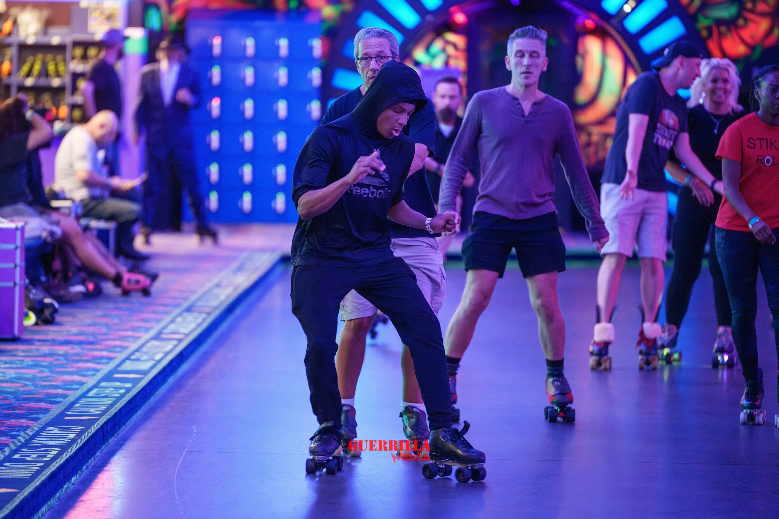 People roller skating in an indoor rink with colorful lighting and a vibrant, neon-themed background.