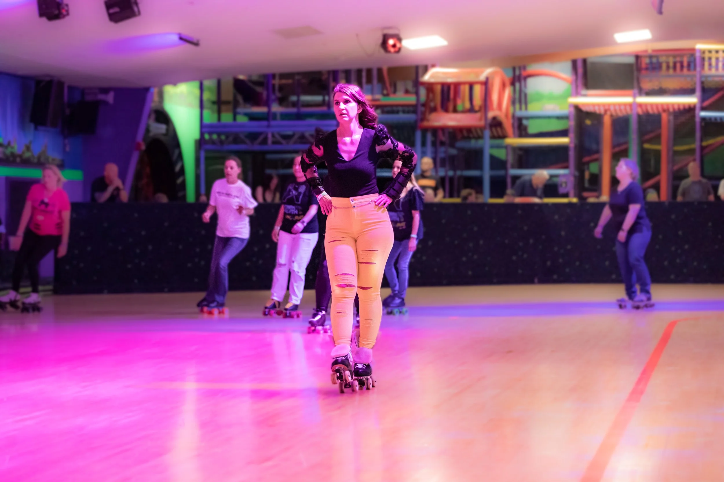 Woman roller skating in an indoor rink with colorful lighting, and other skaters in the background.