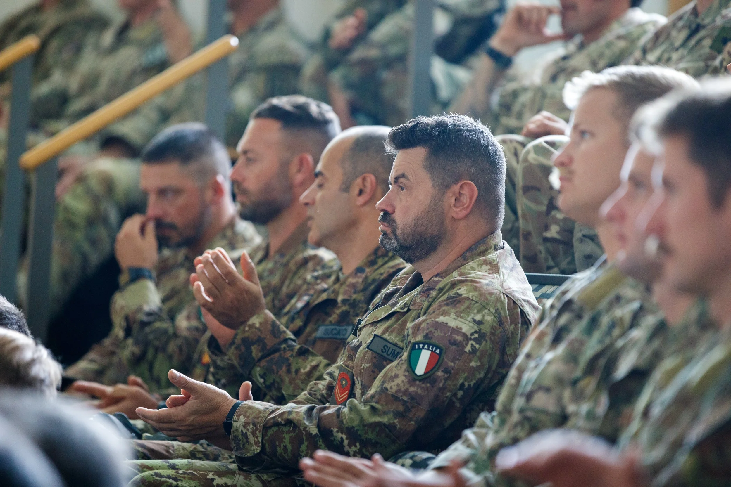 Military personnel sitting in an audience, clapping during a formal event or ceremony.