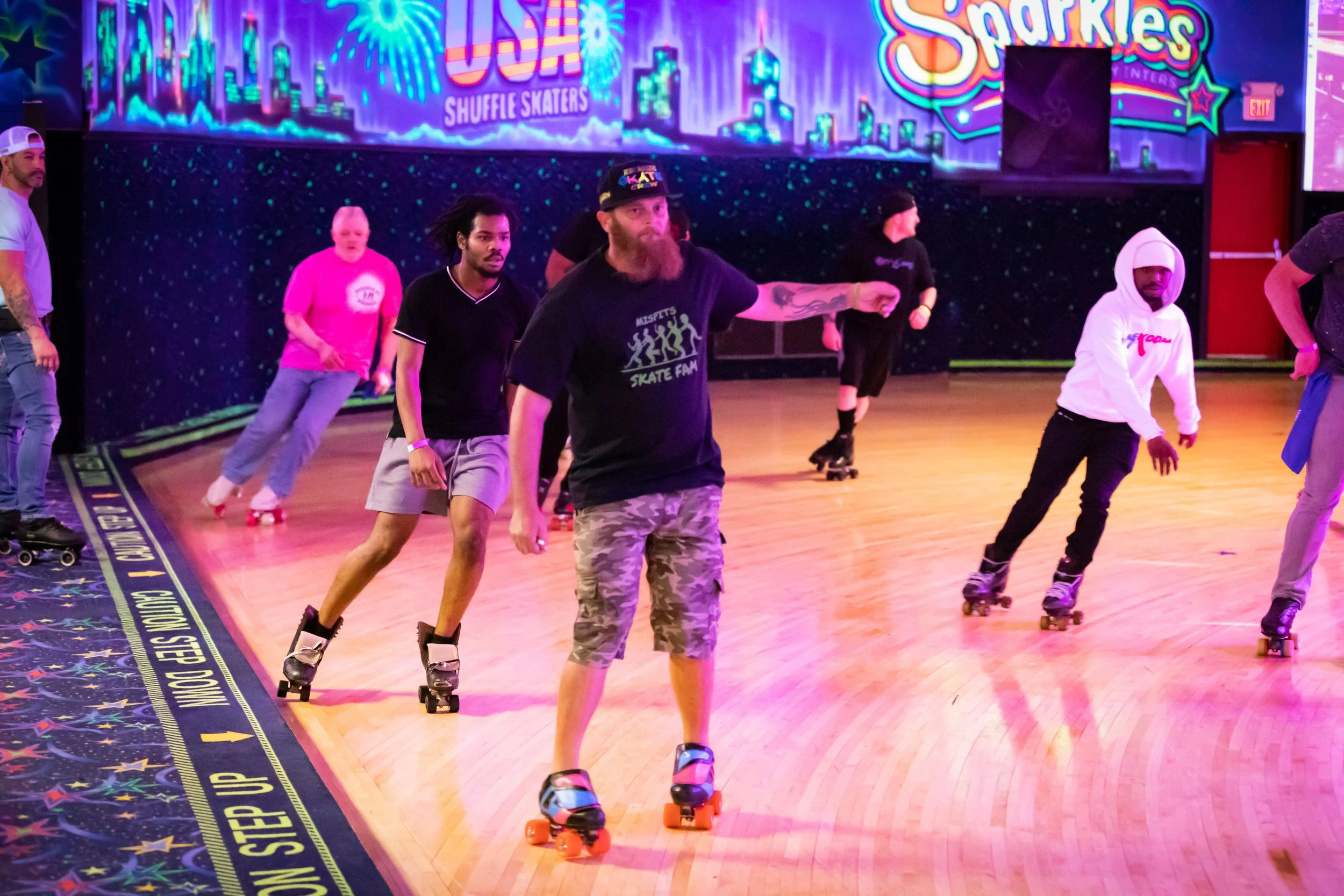 People roller skating in an indoor rink, with colorful neon wall art and a space-themed floor.