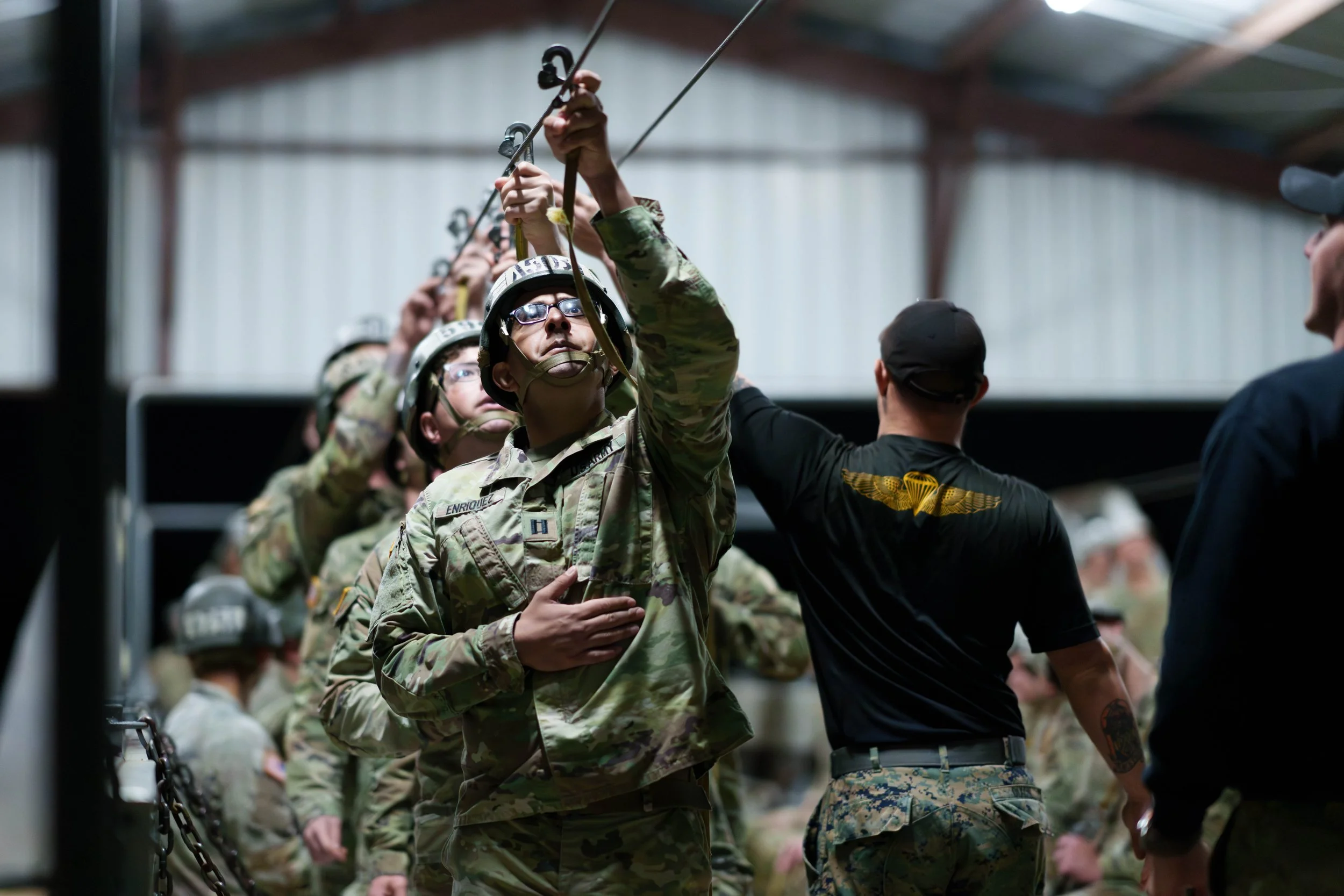 Military personnel in camouflage uniforms during a ceremony or drill, with a focus on a soldier placing a hand over his heart.
