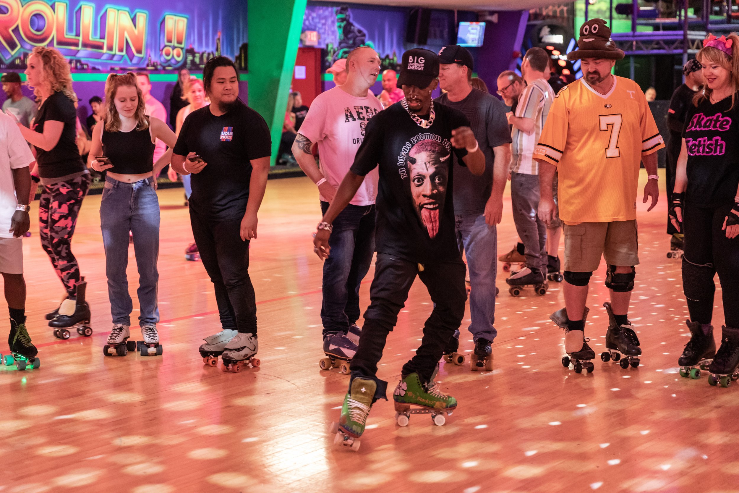 People roller skating in a vibrant indoor roller rink with colorful lights and a mural that says 'Rollin'.