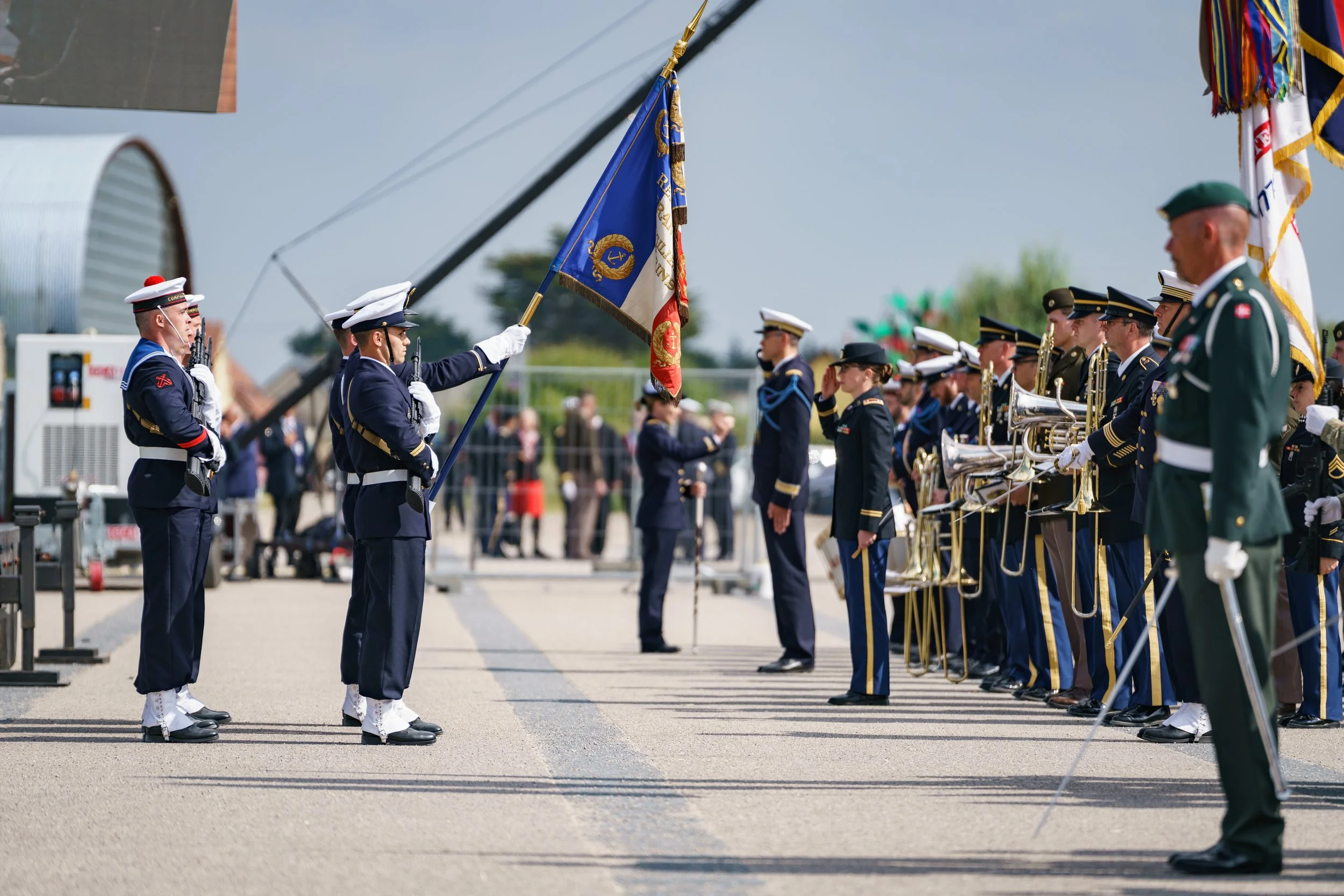 Military personnel in uniform performing a formal ceremony with flags and musical instruments outdoors.