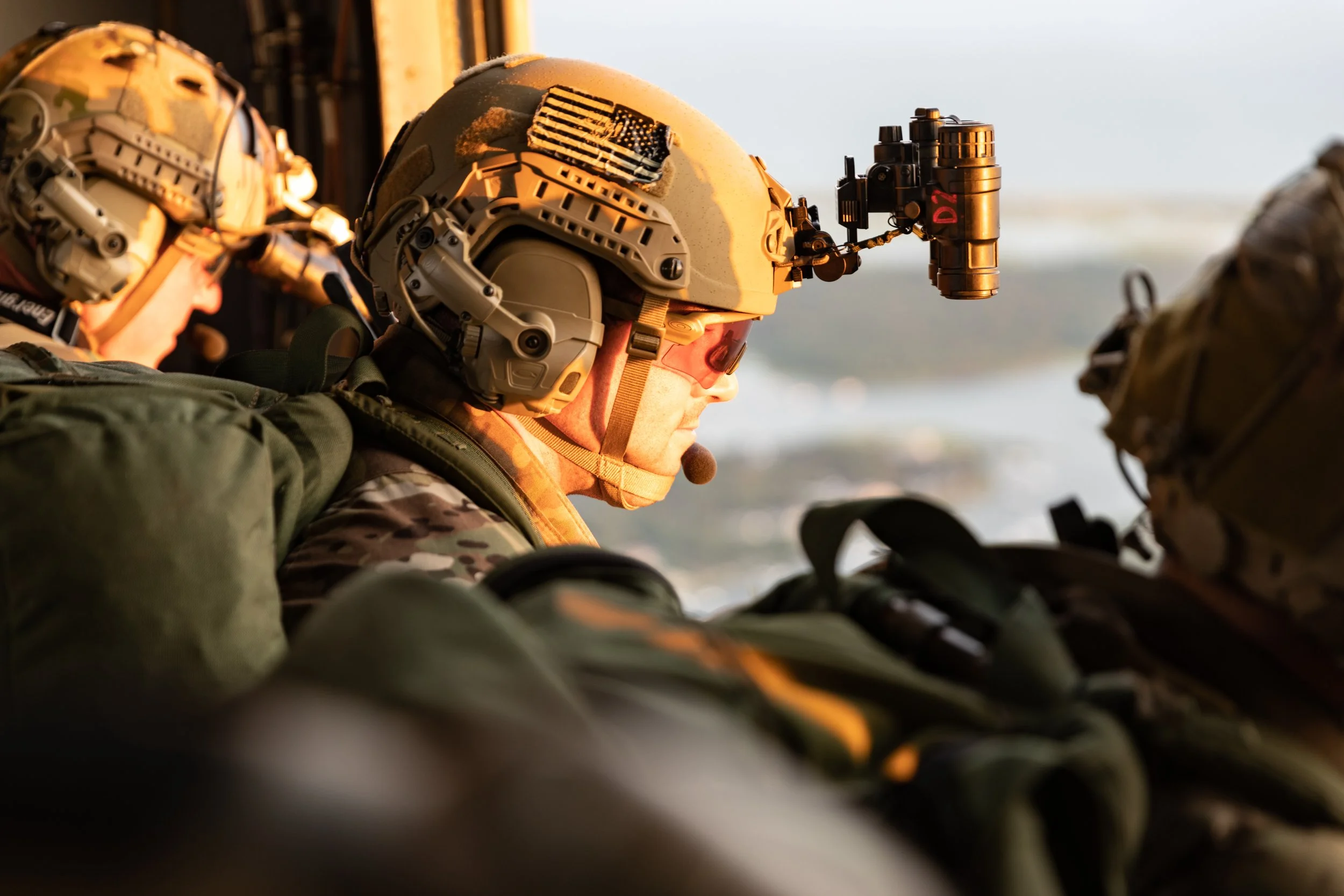 Military personnel wearing tactical gear and helmets, one with a mounted camera, inside a vehicle.