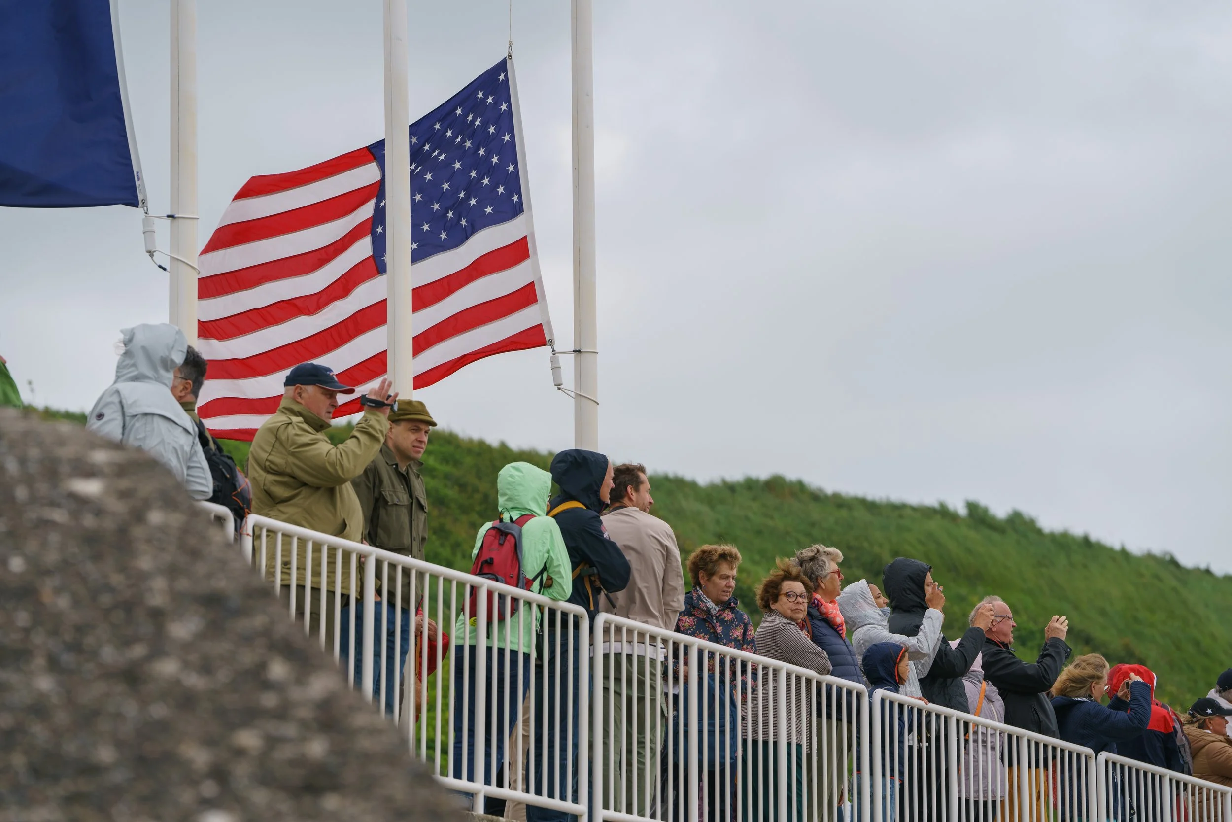 People standing on a white railing on a cloudy day, with American flags waving in the background.
