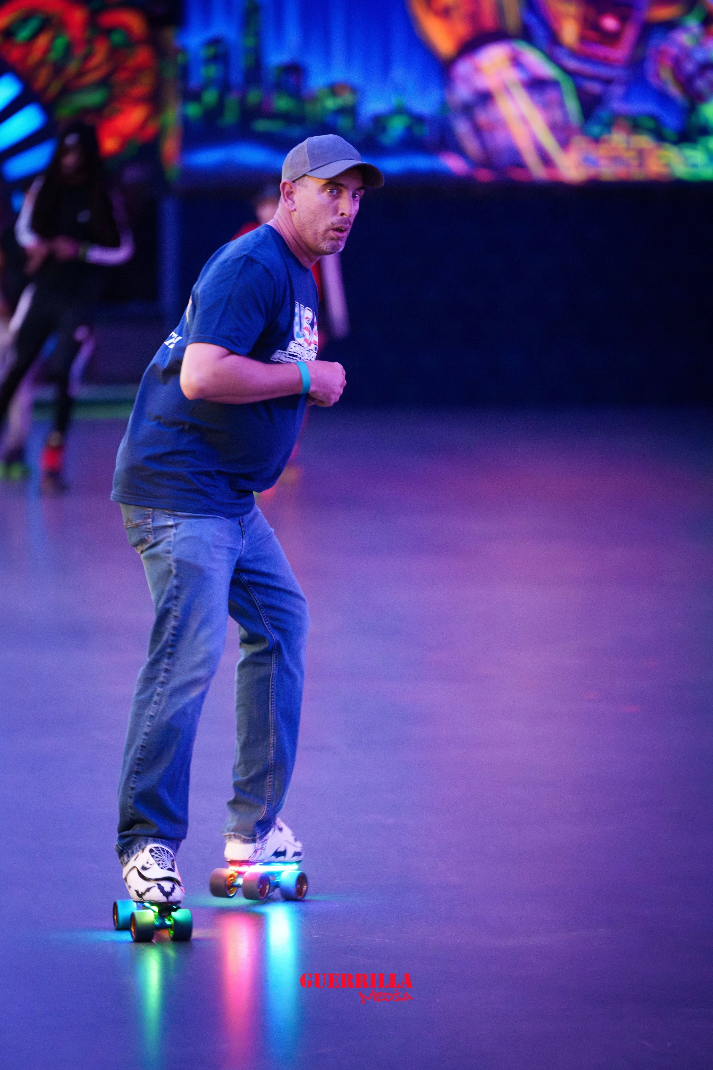 A man roller skating in an indoor rink with colorful neon lighting and graffiti-style artwork on the wall in the background.