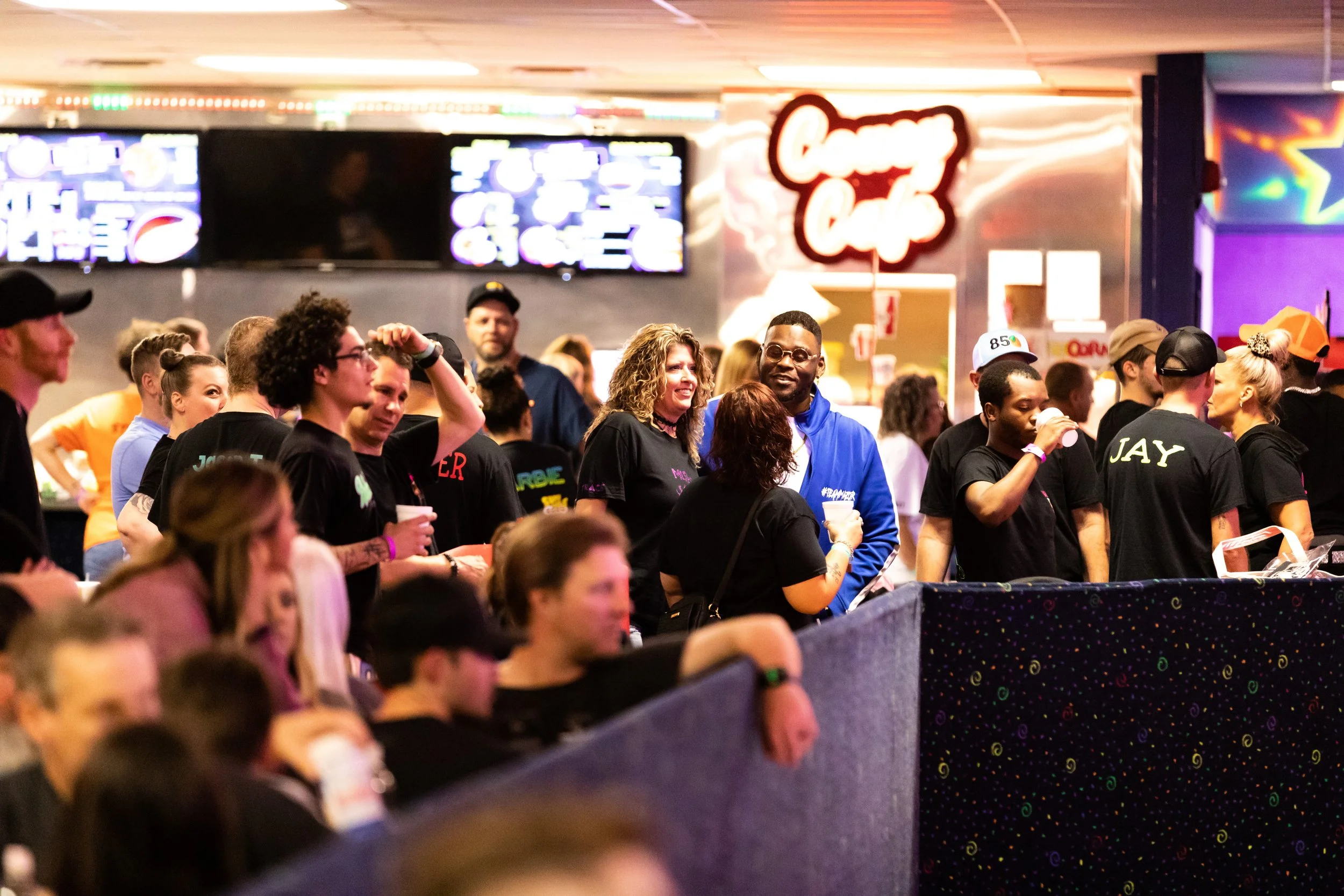 People standing in line at a food court, waiting to order food, with a smiling woman and man talking in the center, surrounded by others ordering and socializing.
