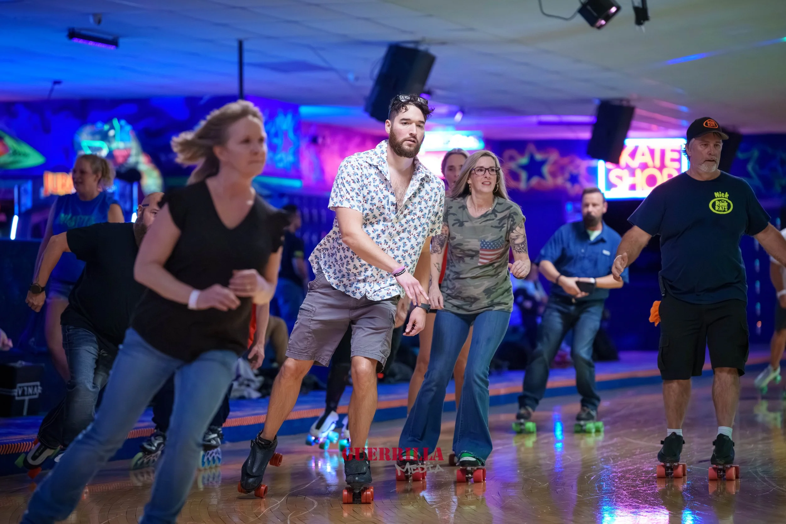 Group of people roller skating in a roller rink with colorful neon lights and a sign that says 'KATE SHOP' in the background.