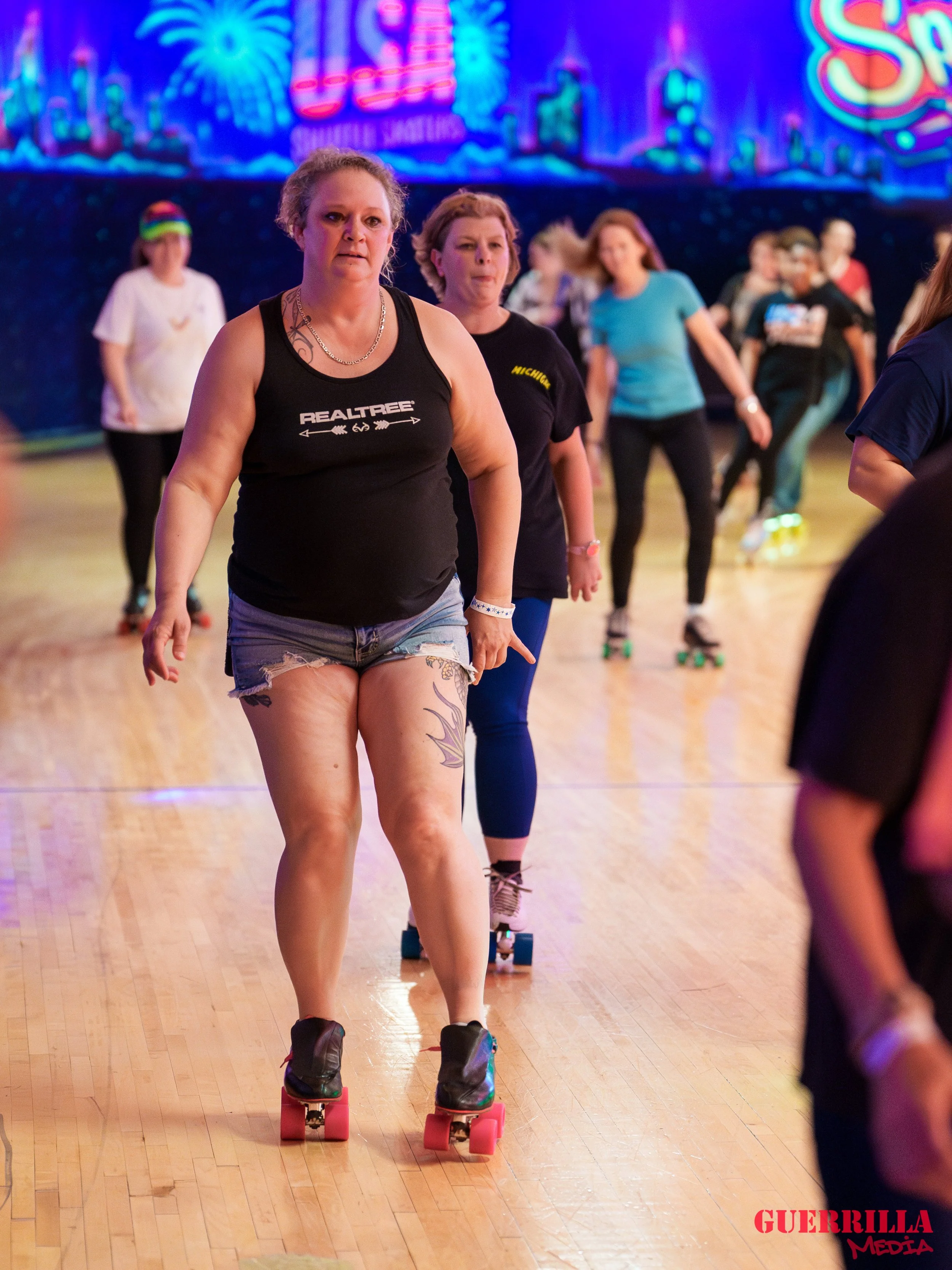 Multiple women roller skating indoors with neon signs and colorful lights in the background.