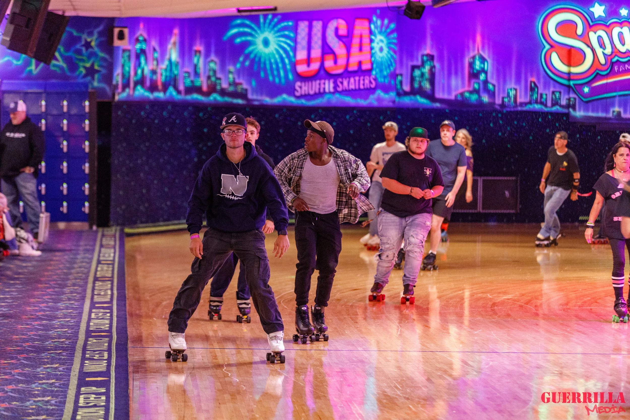 People roller skating at an indoor rink with colorful lighting and a sign that reads 'USA Shuffle Skaters'.