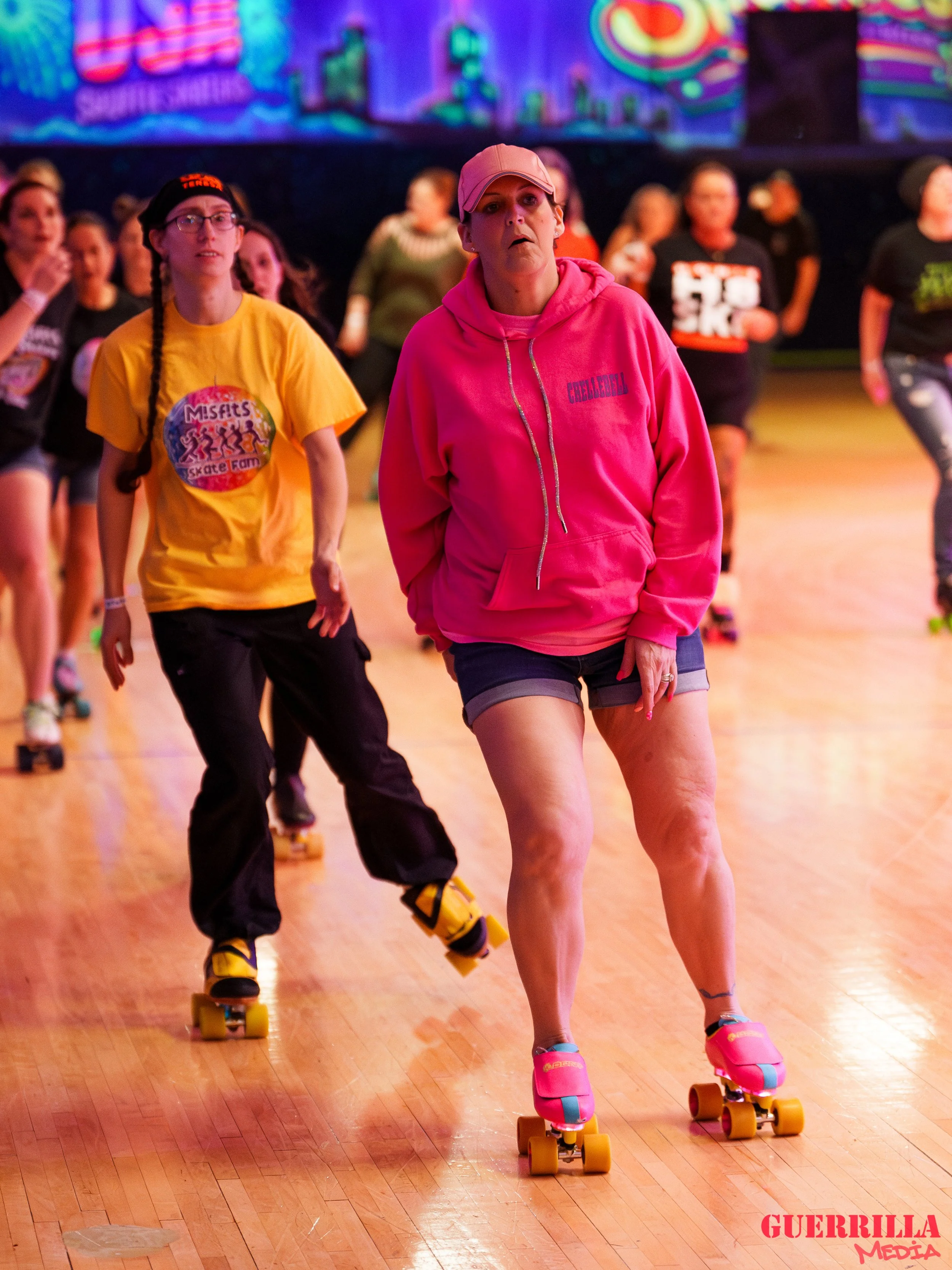 Women roller skating indoors with a colorful background, wearing casual athletic clothing.