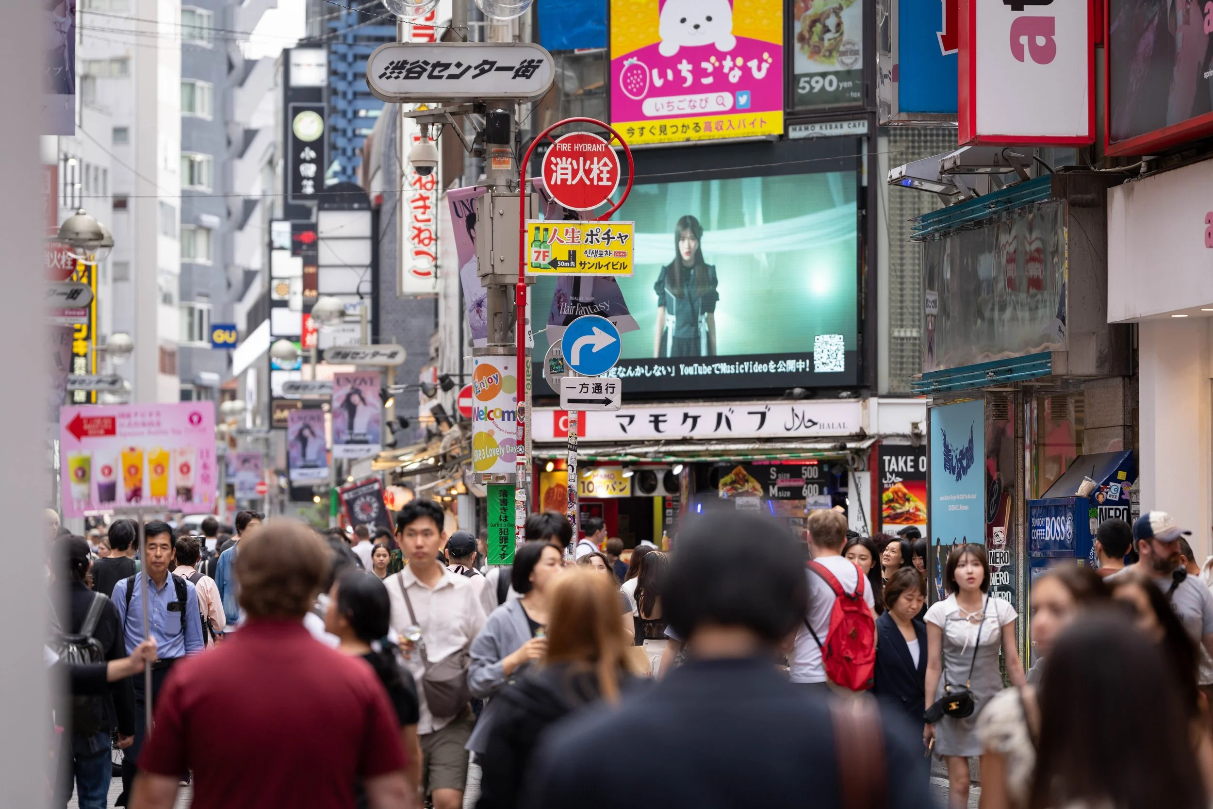A busy street scene in Japan with many pedestrians, colorful signs, and electronic billboards in the background.