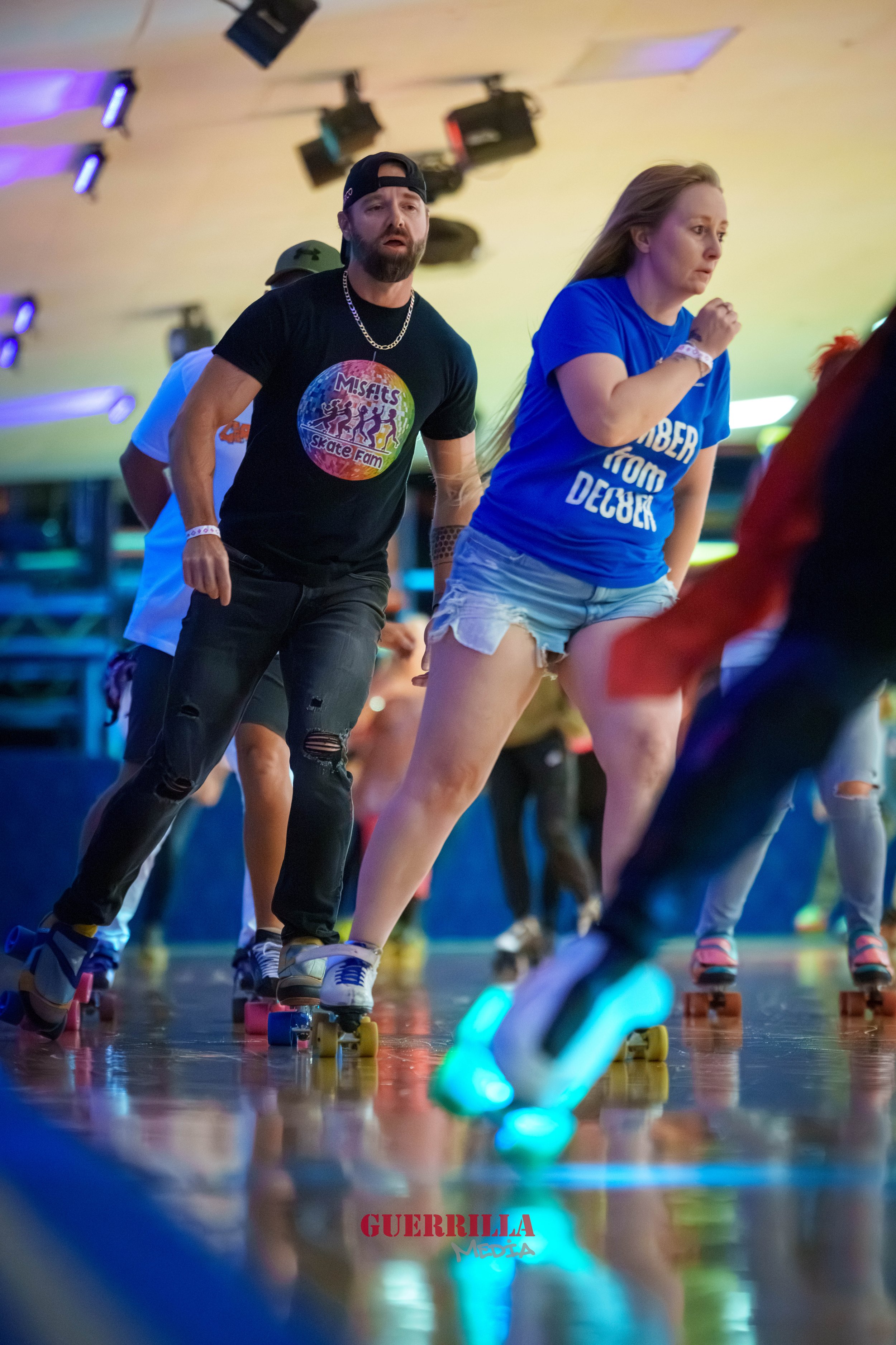 People roller skating at an indoor skating rink, some wearing casual clothes and wristbands, under colorful lighting with a wooden floor and ceiling lights.