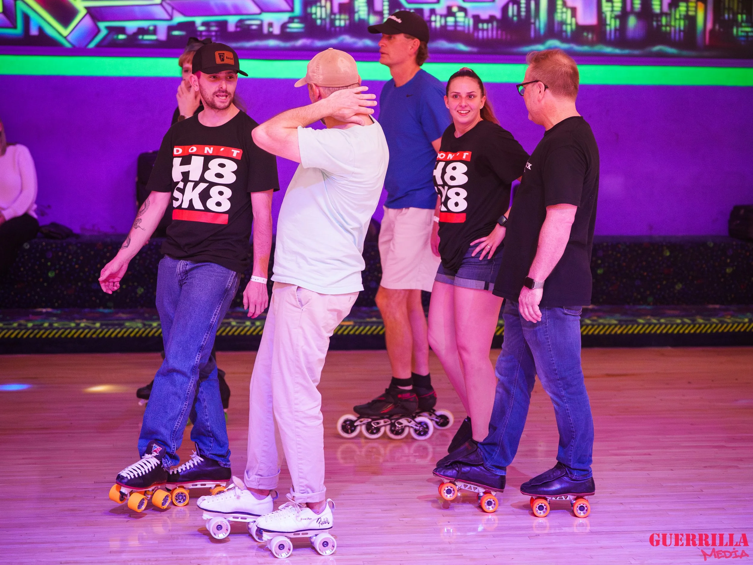 Six people are roller skating indoors under colorful neon lights, with three wearing black shirts with 