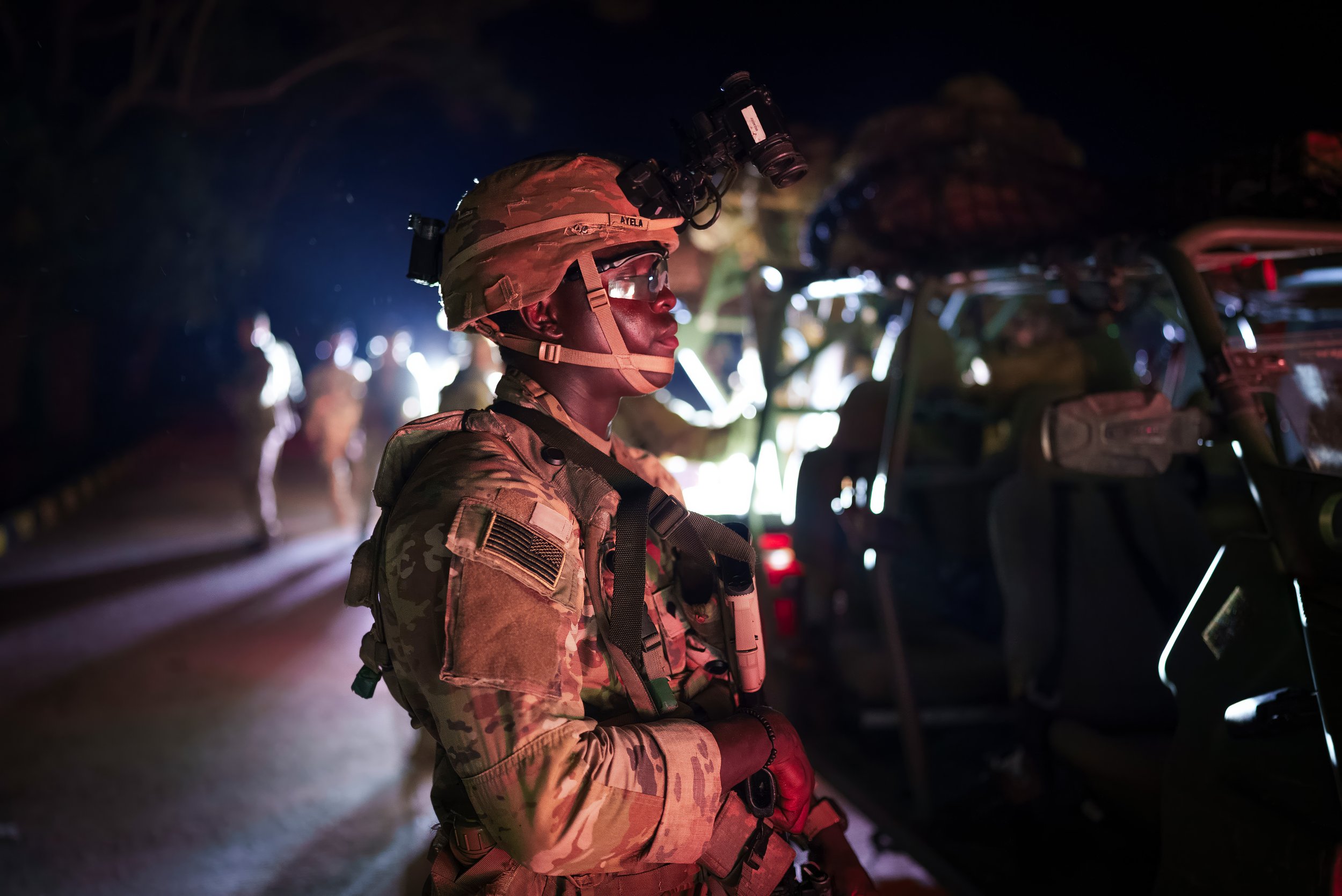 Military personnel in uniform standing near military vehicles at night during a nighttime operation.