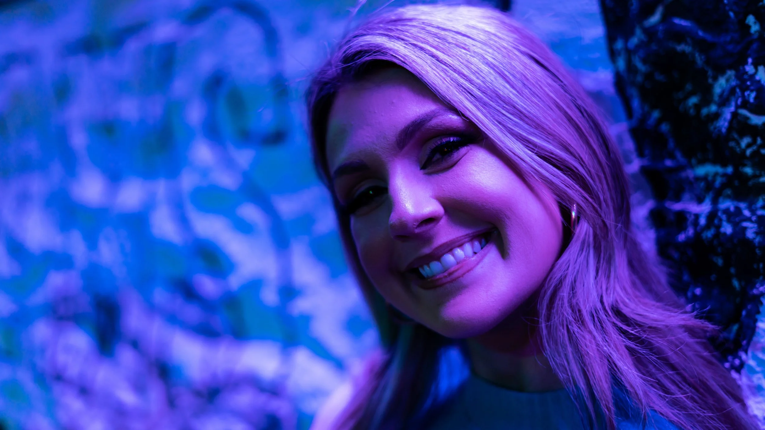 Close-up of a woman smiling with purple and blue lighting reflecting on her face and hair.