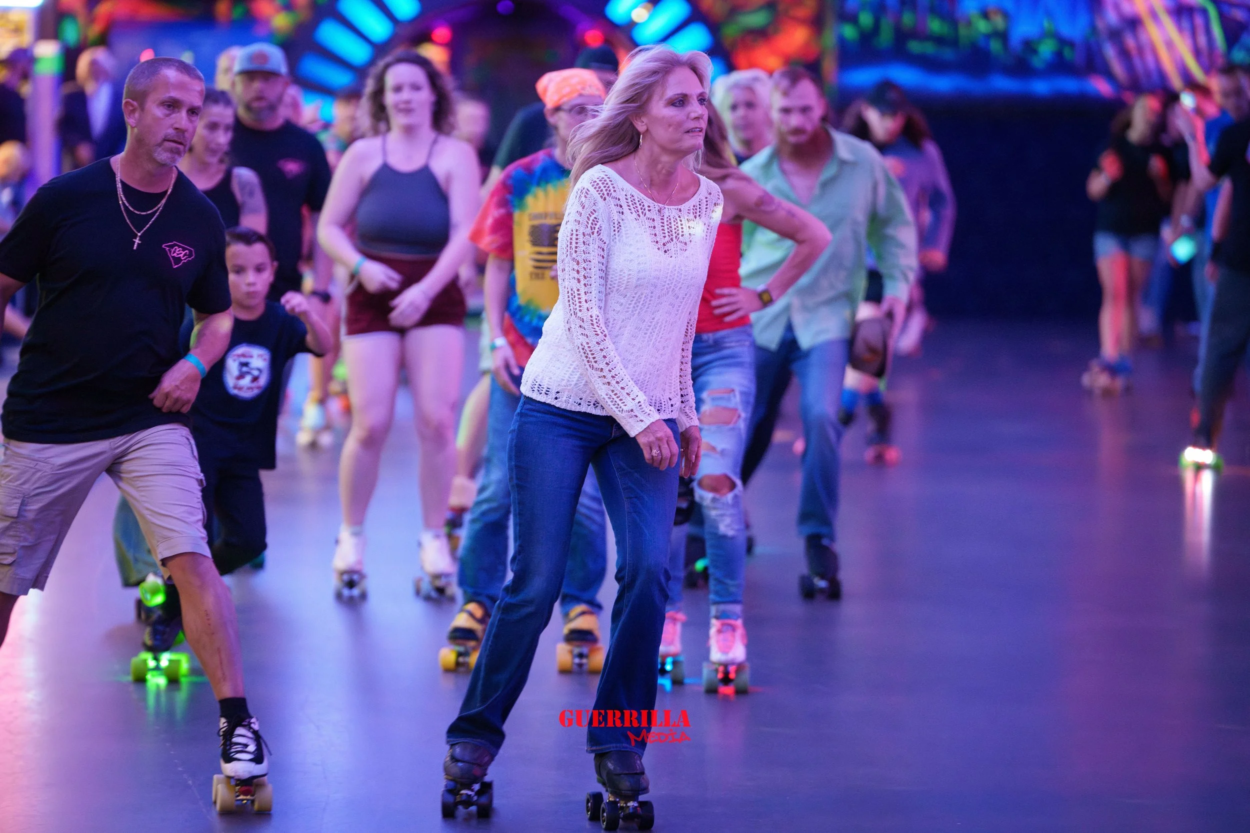 People roller skating in a colorful indoor roller rink, with neon lights and rainbow condpsy fueled background.