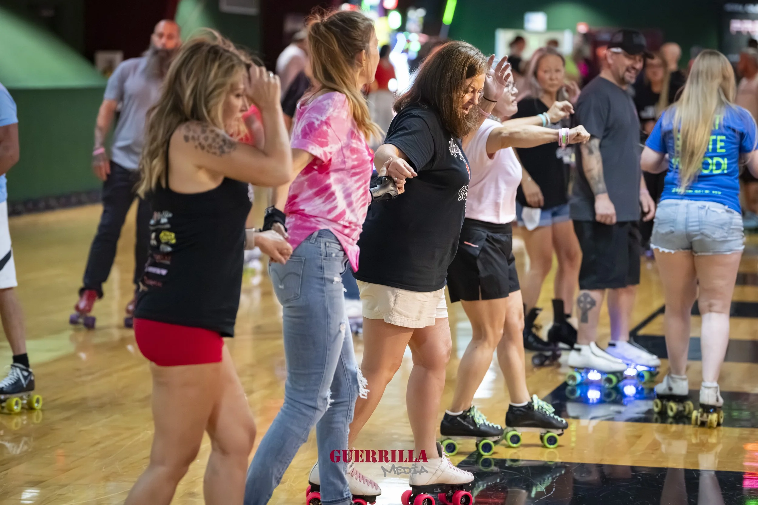Group of people roller skating together indoors, holding hands and smiling.