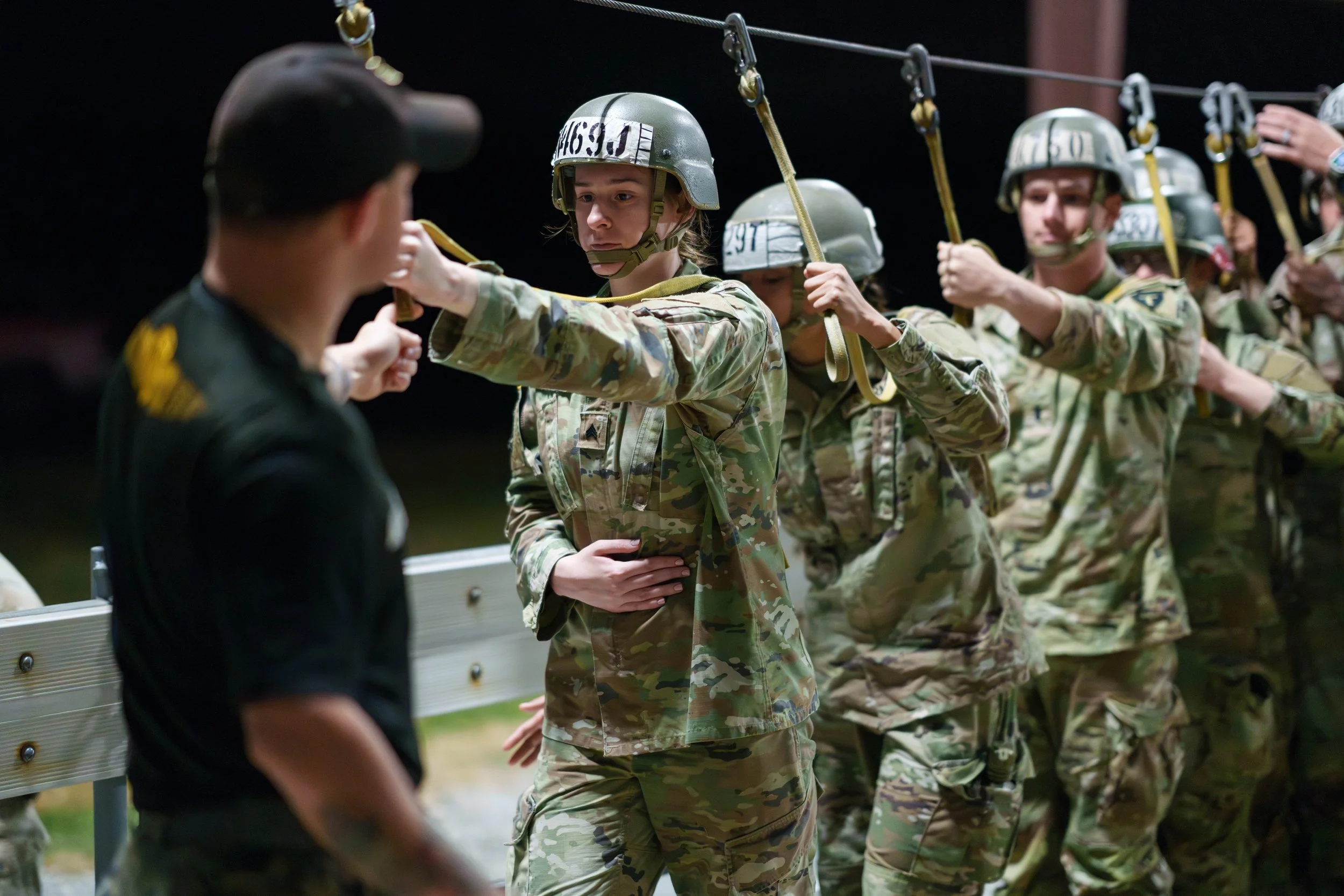 Young soldiers in camouflage uniforms and helmets participating in a military training exercise, handing over a rope or cable in a night training session.