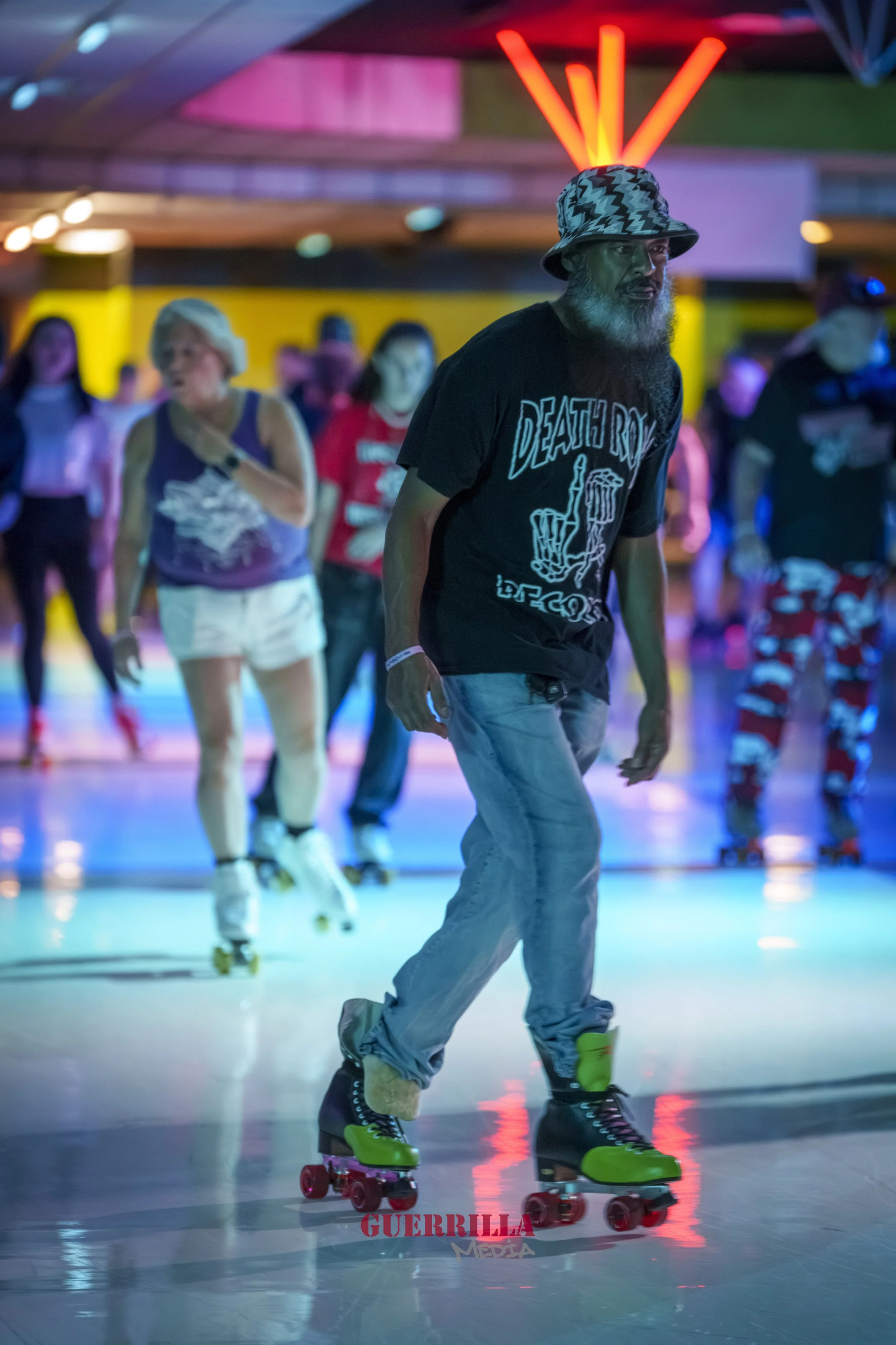 Man roller skating at an indoor roller rink with neon lighting, people in the background skating, and a neon sign overhead.