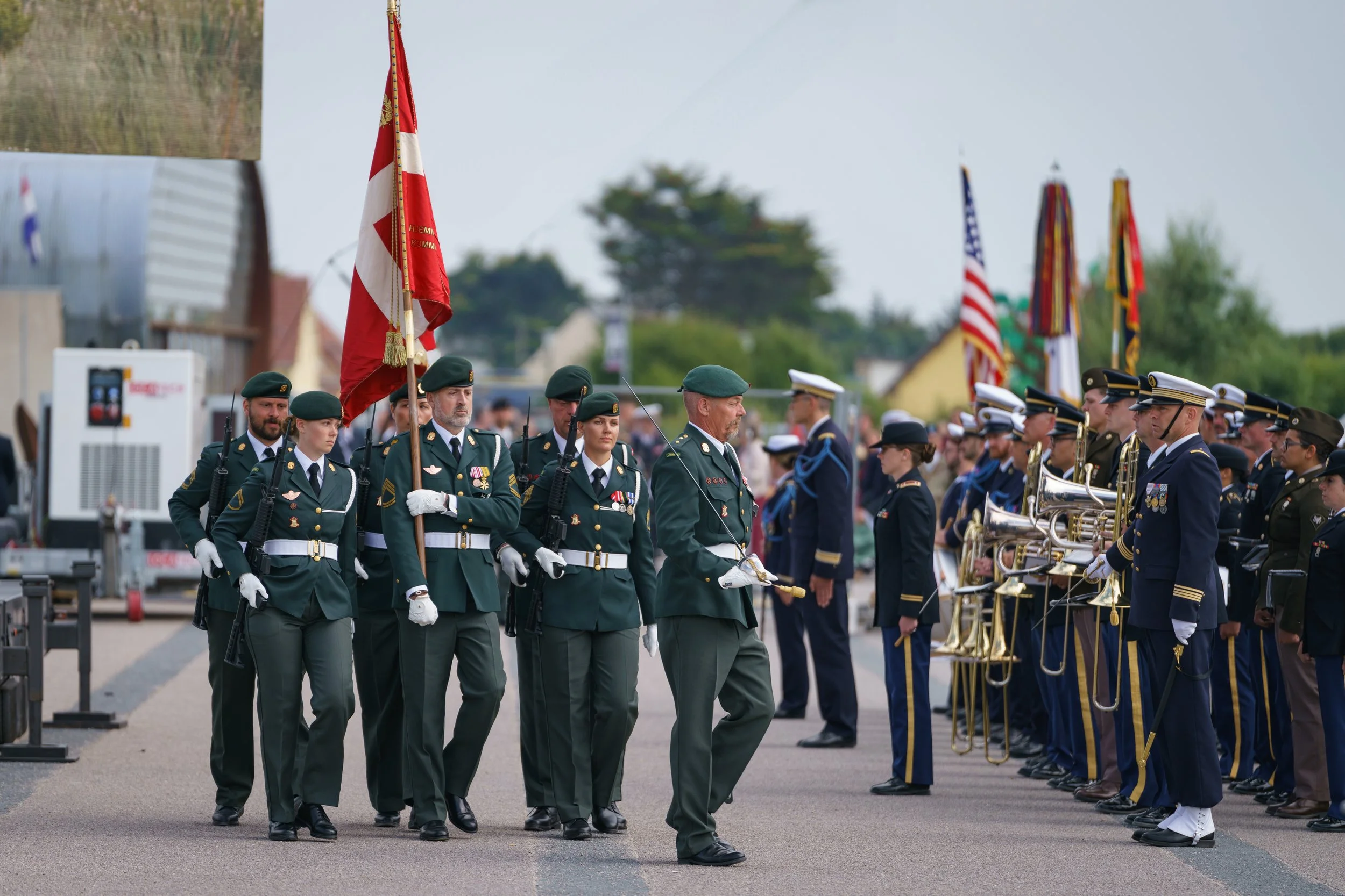 Military personnel marching and standing in formation during a parade or ceremony, with flag bearers carrying national and military flags.
