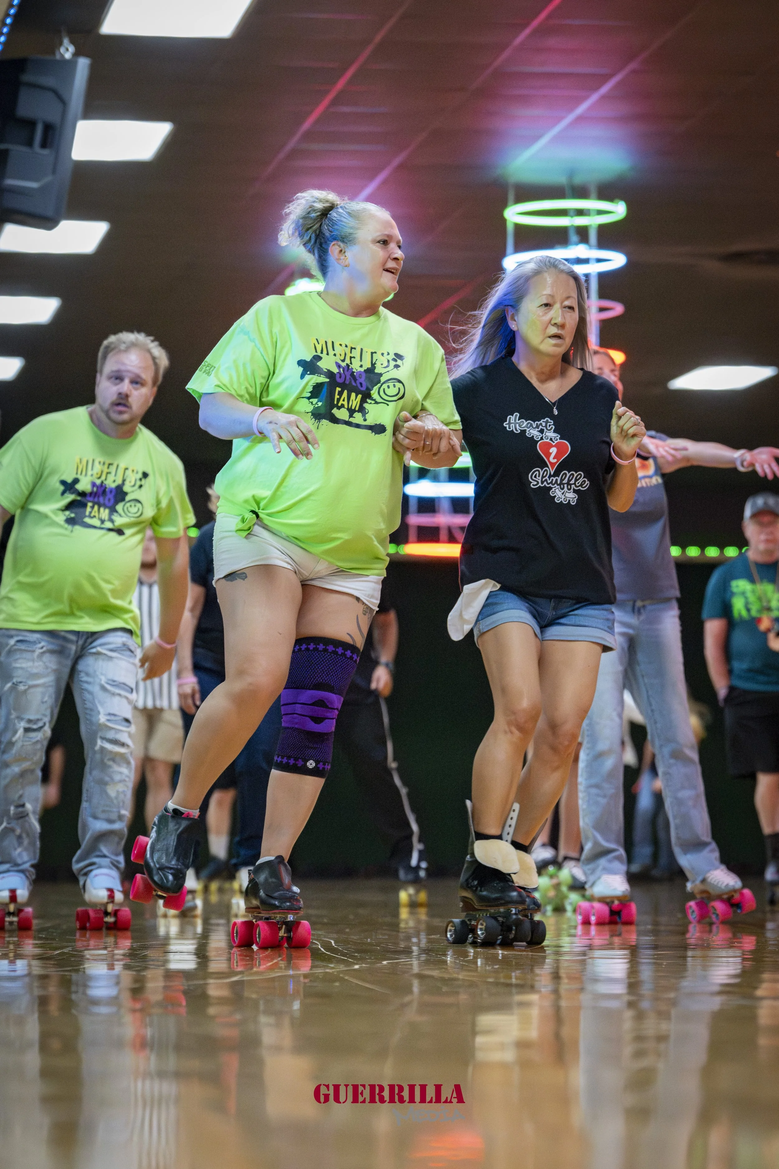 People roller skating at an indoor roller rink with colorful neon lights in the background, wearing casual clothes.