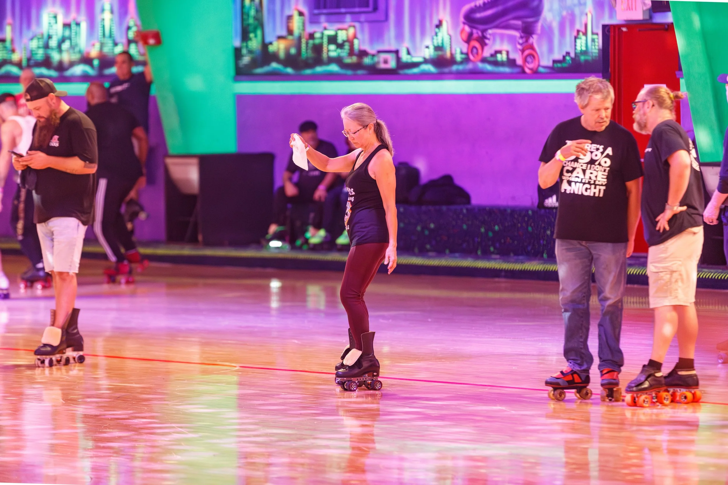 People roller skating indoors with colorful neon cityscape mural on the wall in the background.