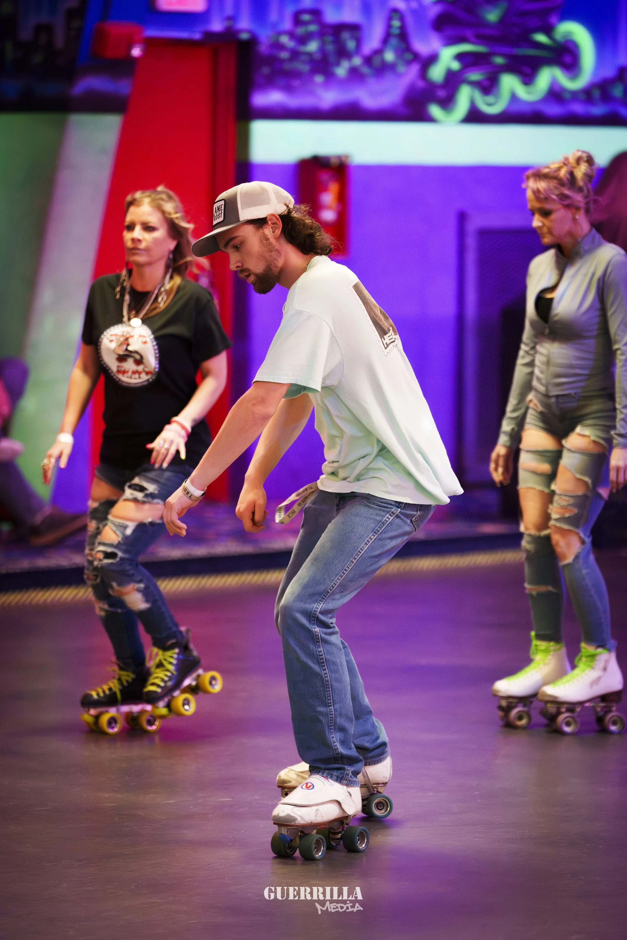 People roller skating indoors with colorful neon lights and urban art in the background.