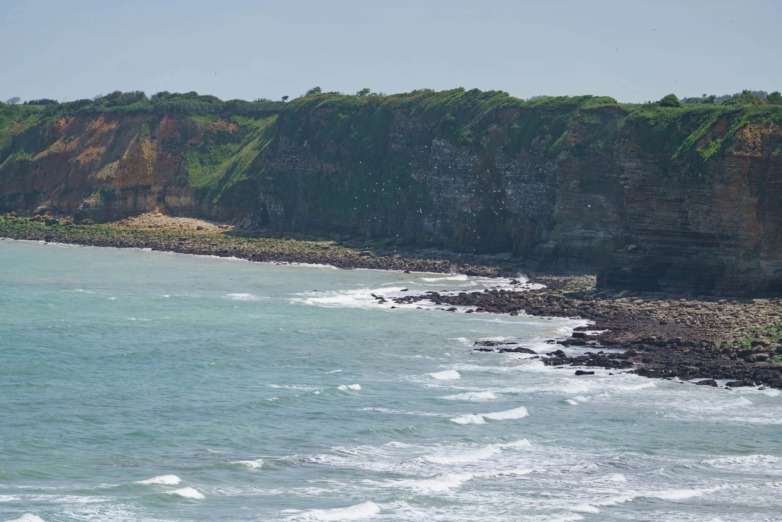 Scenic view of a coastline with green cliffs and waves crashing on rocks along the shore.