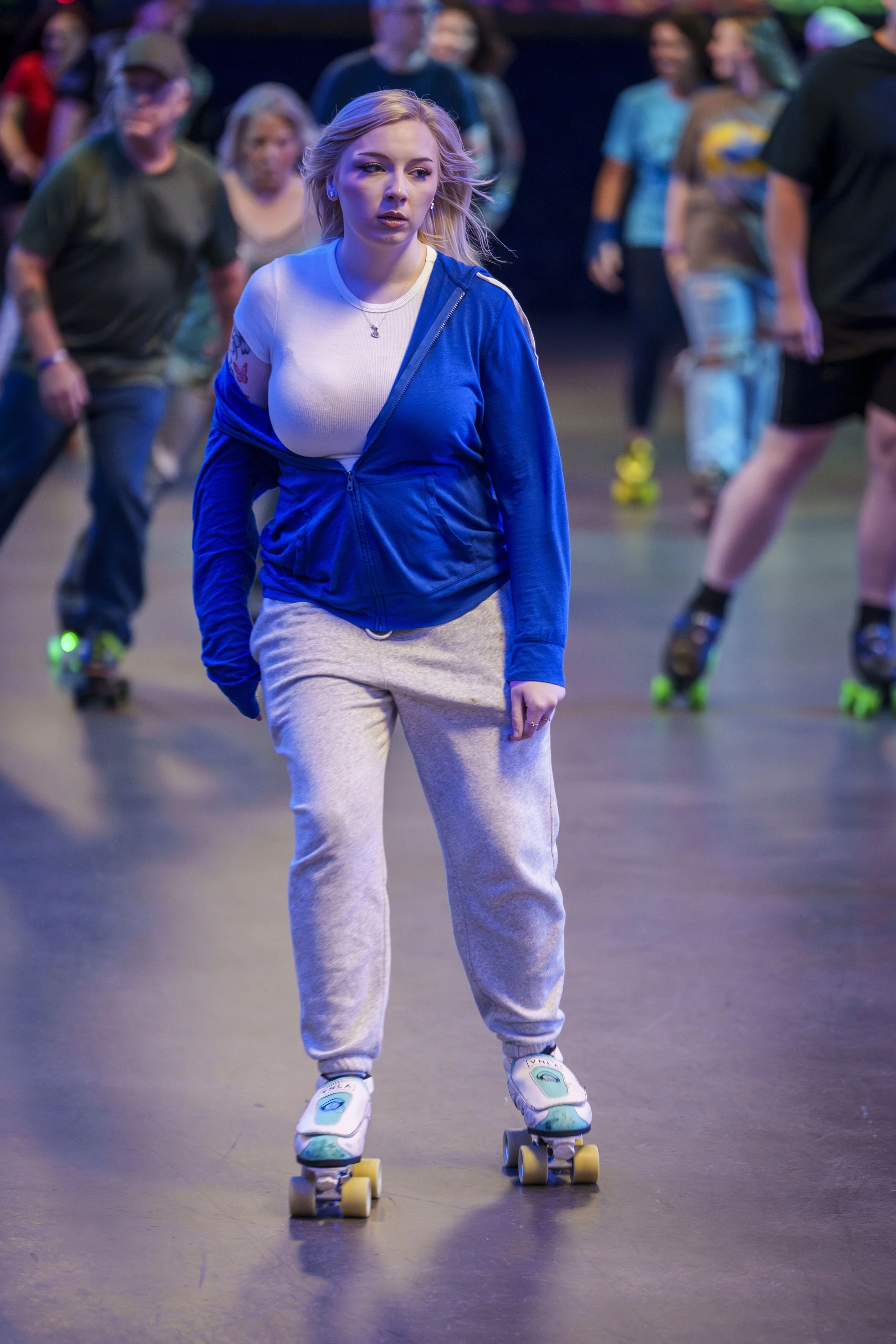 A young woman roller skating in an indoor rink with other skaters in the background.