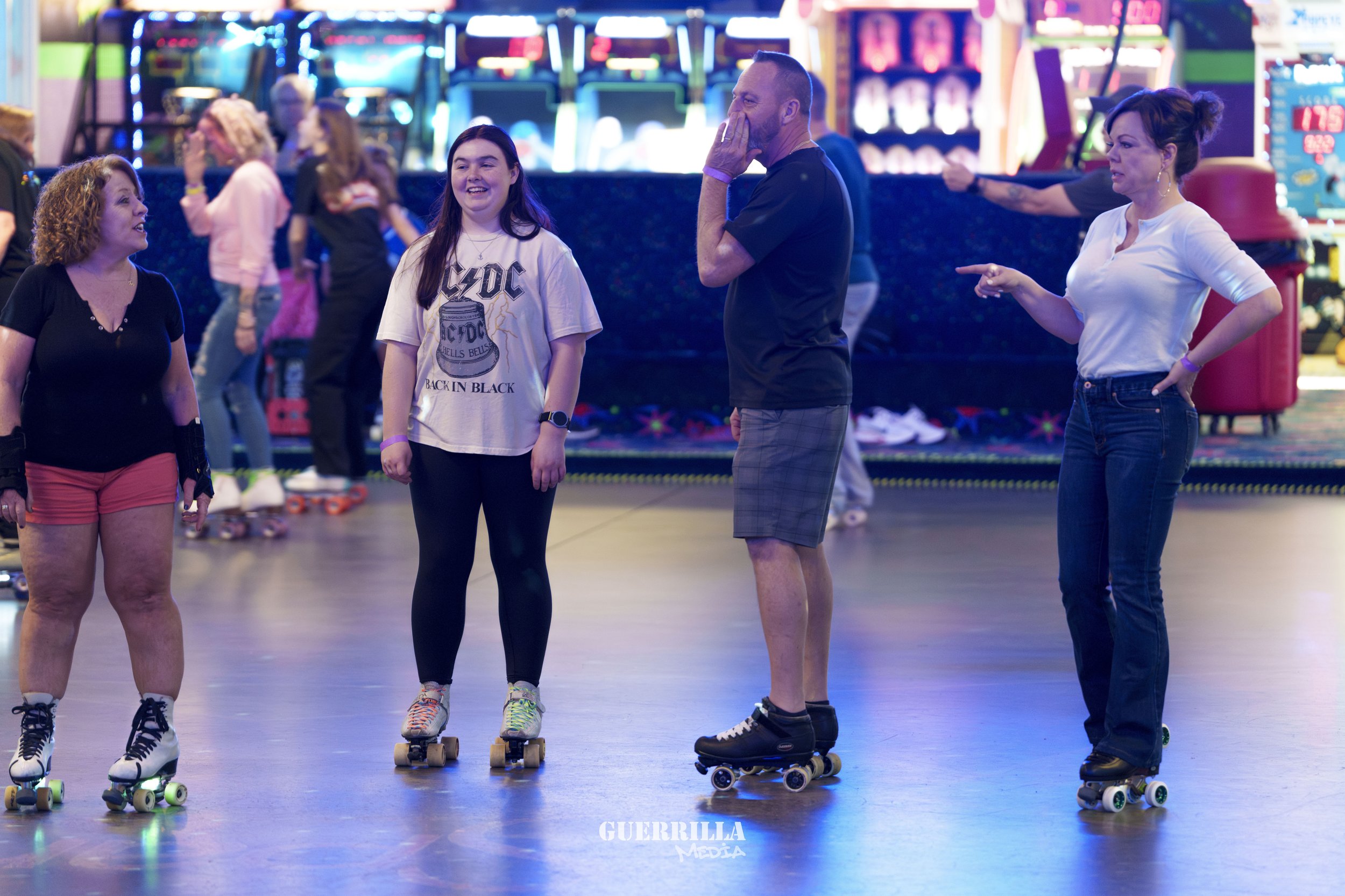 Four people roller skating inside an arcade, two women and one man in the foreground, with other skaters and arcade machines visible in the background.