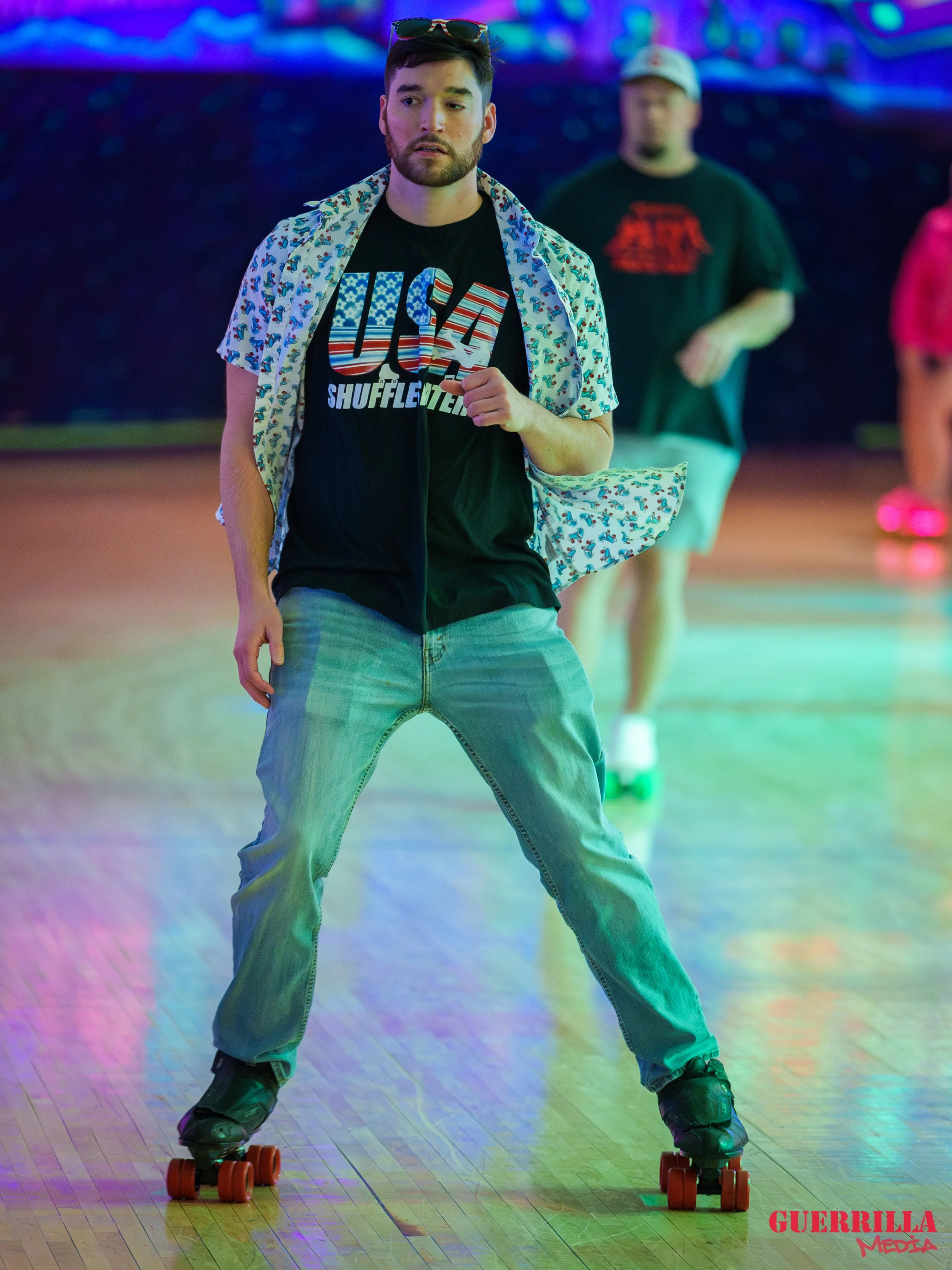 A man roller skating on a rink with colorful lighting and a man in the background.