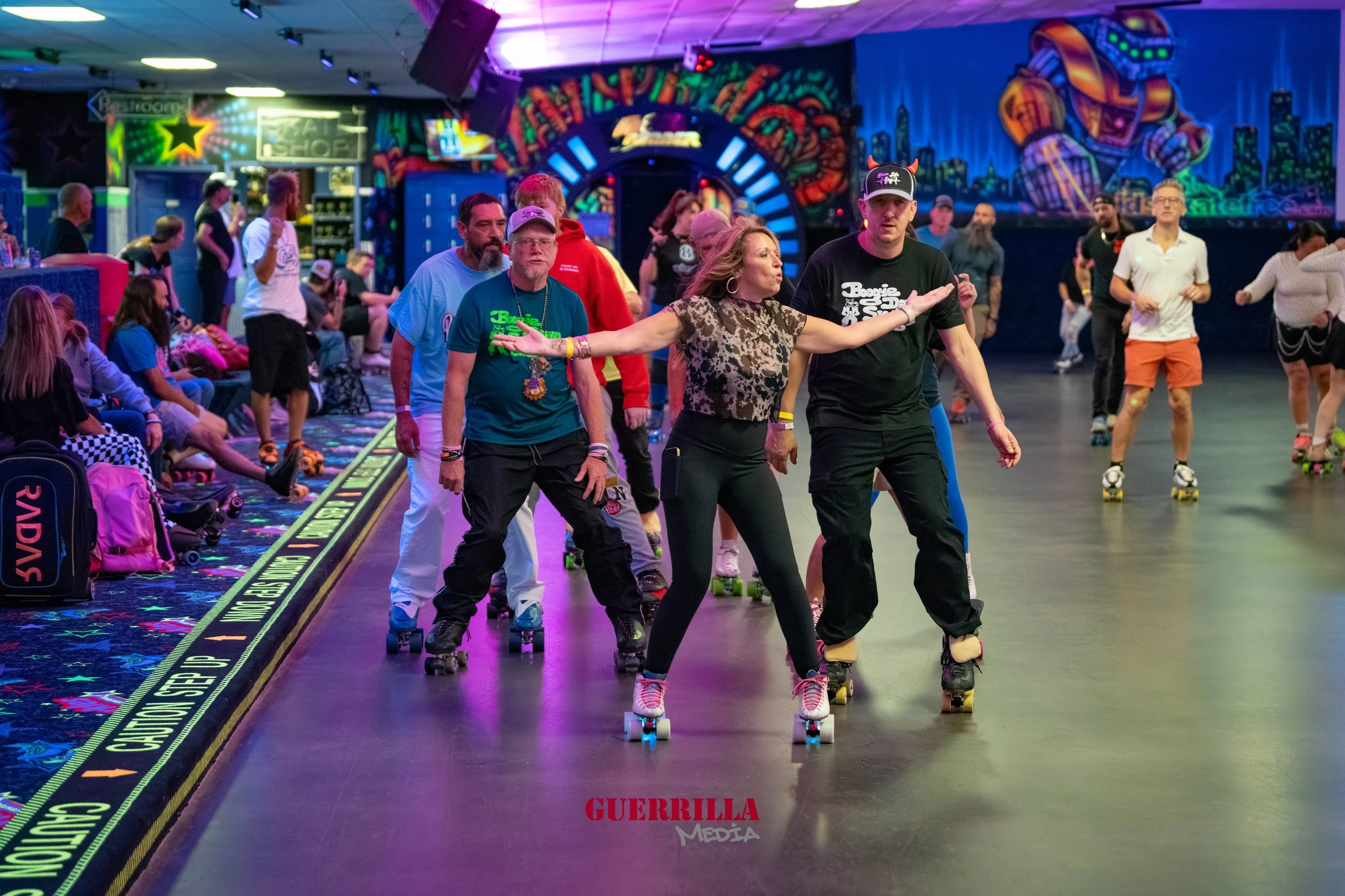 People roller skating in an indoor roller rink with colorful neon lights and graffiti art on the walls. A woman in a leopard print top is dancing with arms outstretched, surrounded by other skaters and spectators.