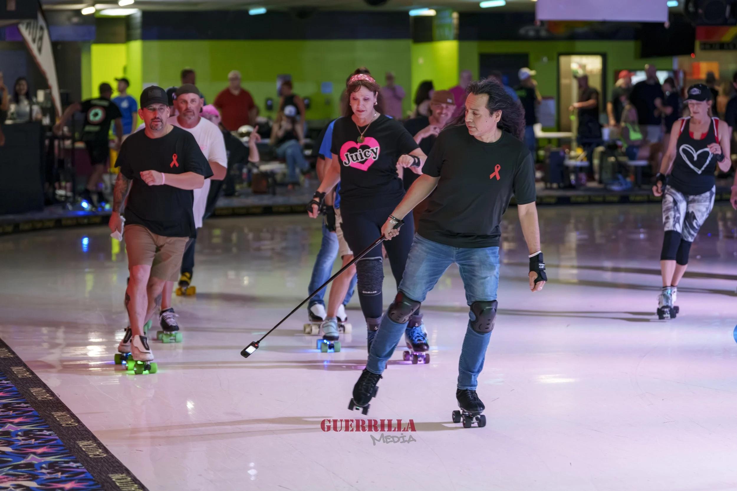 People roller skating indoors, some with protective gear, in a roller rink with colorful lights and a green wall in the background.