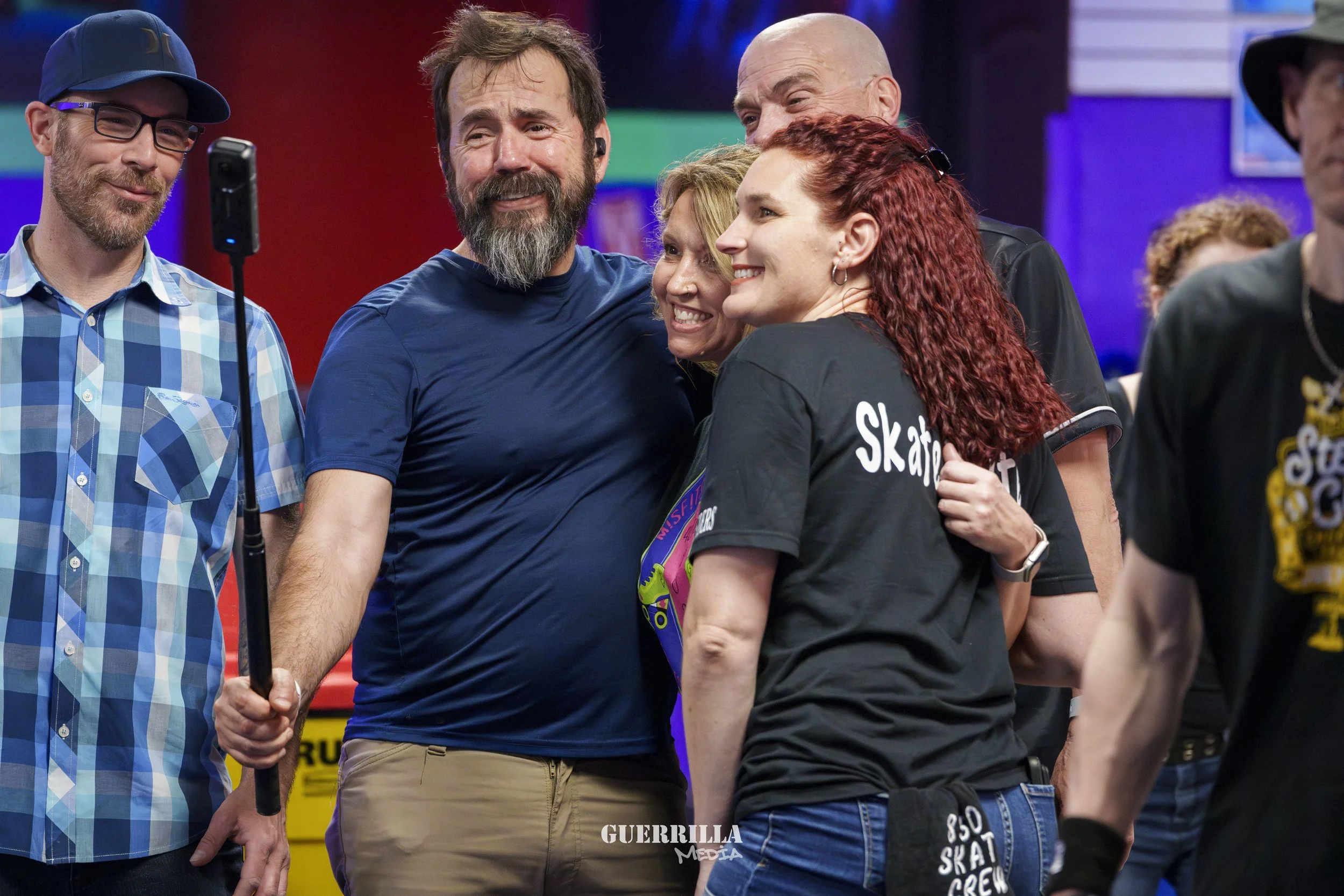 Group of people taking a selfie at an event, with colorful banners and posters in the background.