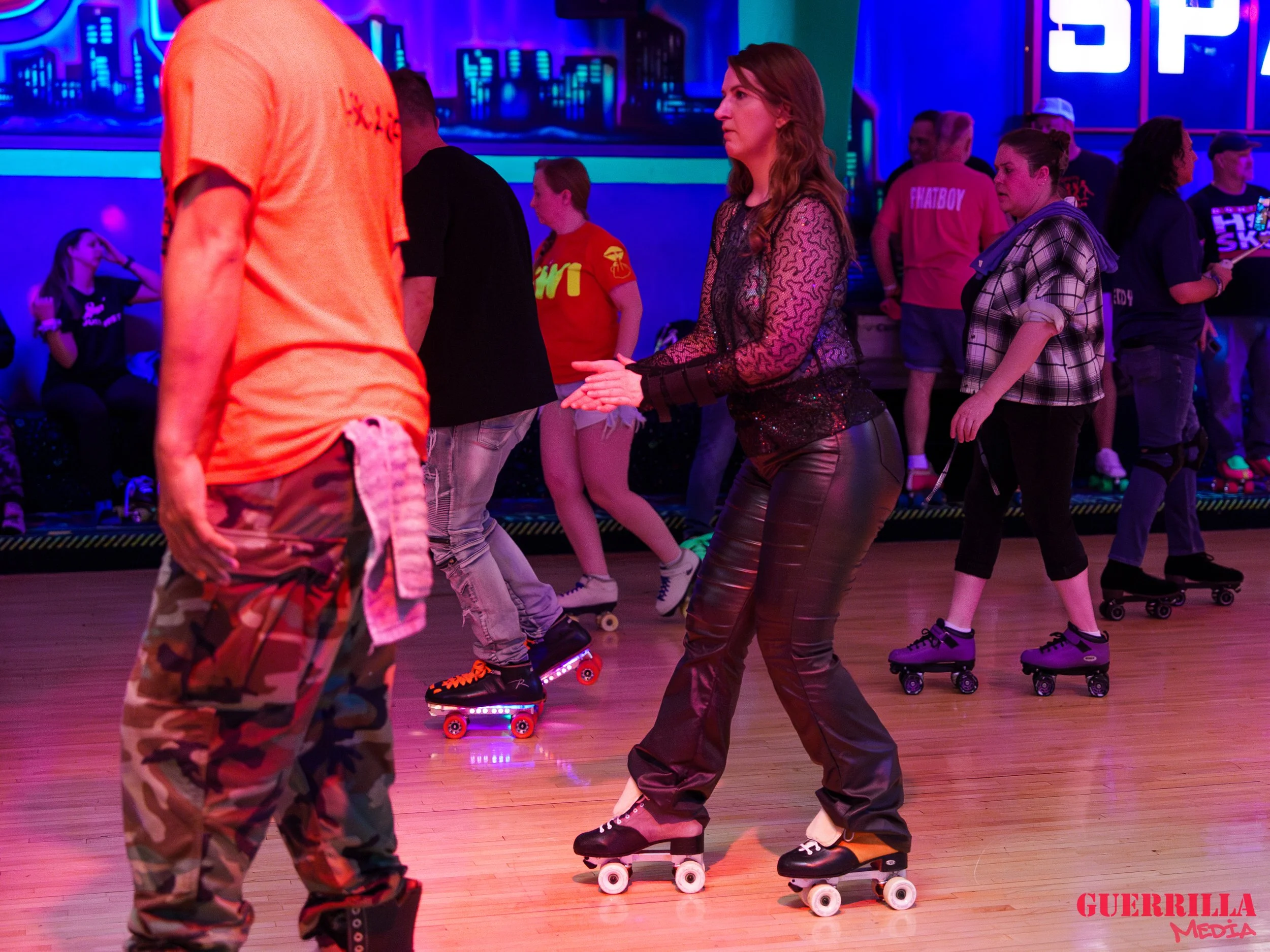 People roller skating in an indoor rink illuminated with colorful neon lights.
