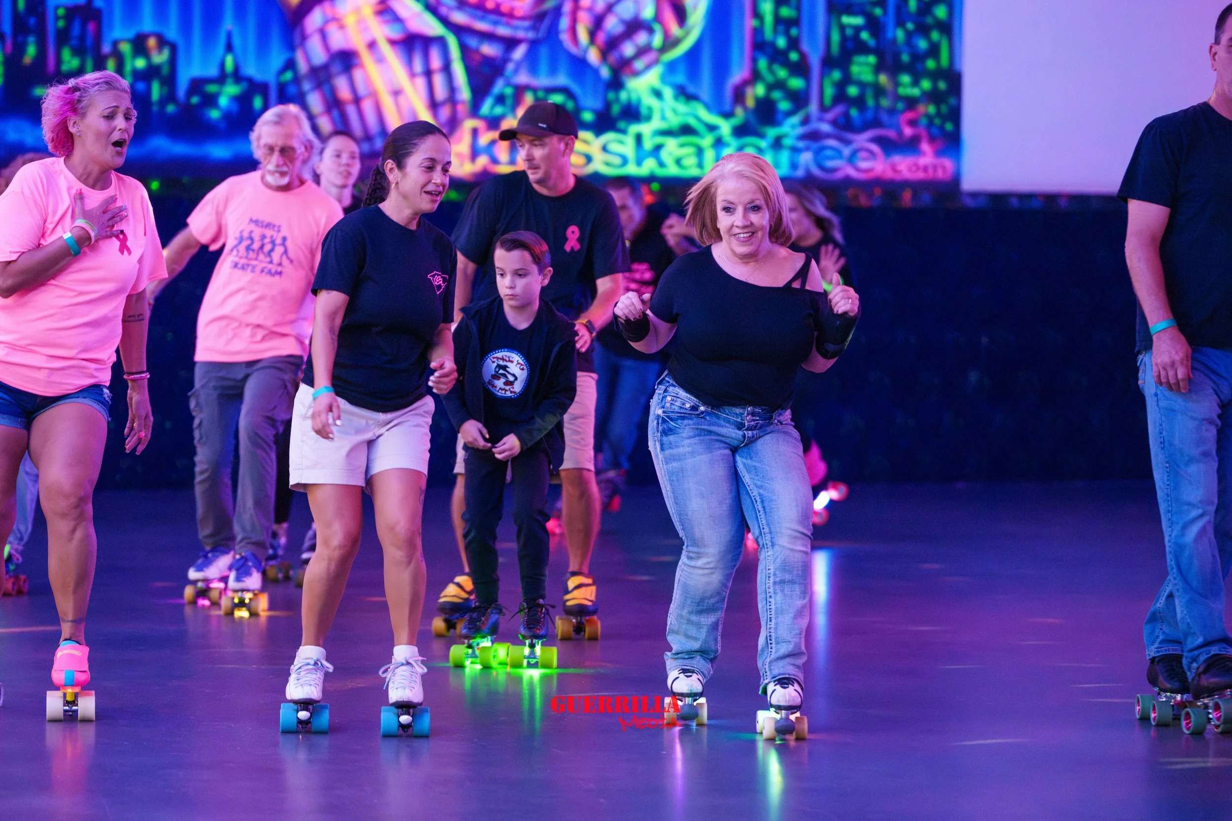 People roller skating indoors, participating in a dance or exercise event, with a colorful vibrant background and the word 'GUERRILLA' visible.