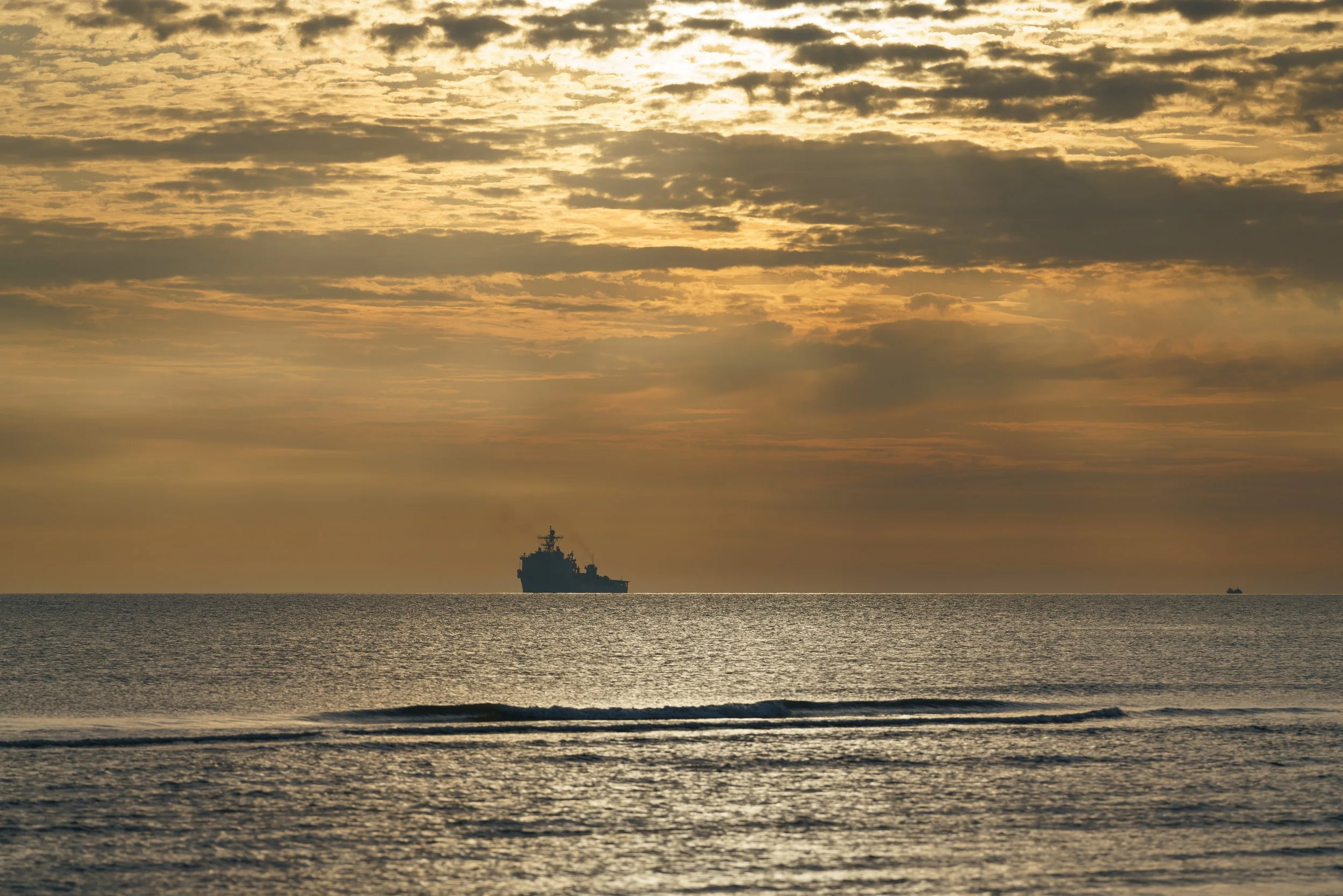 Sunset over the ocean with a ship in the distance and clouds in the sky.