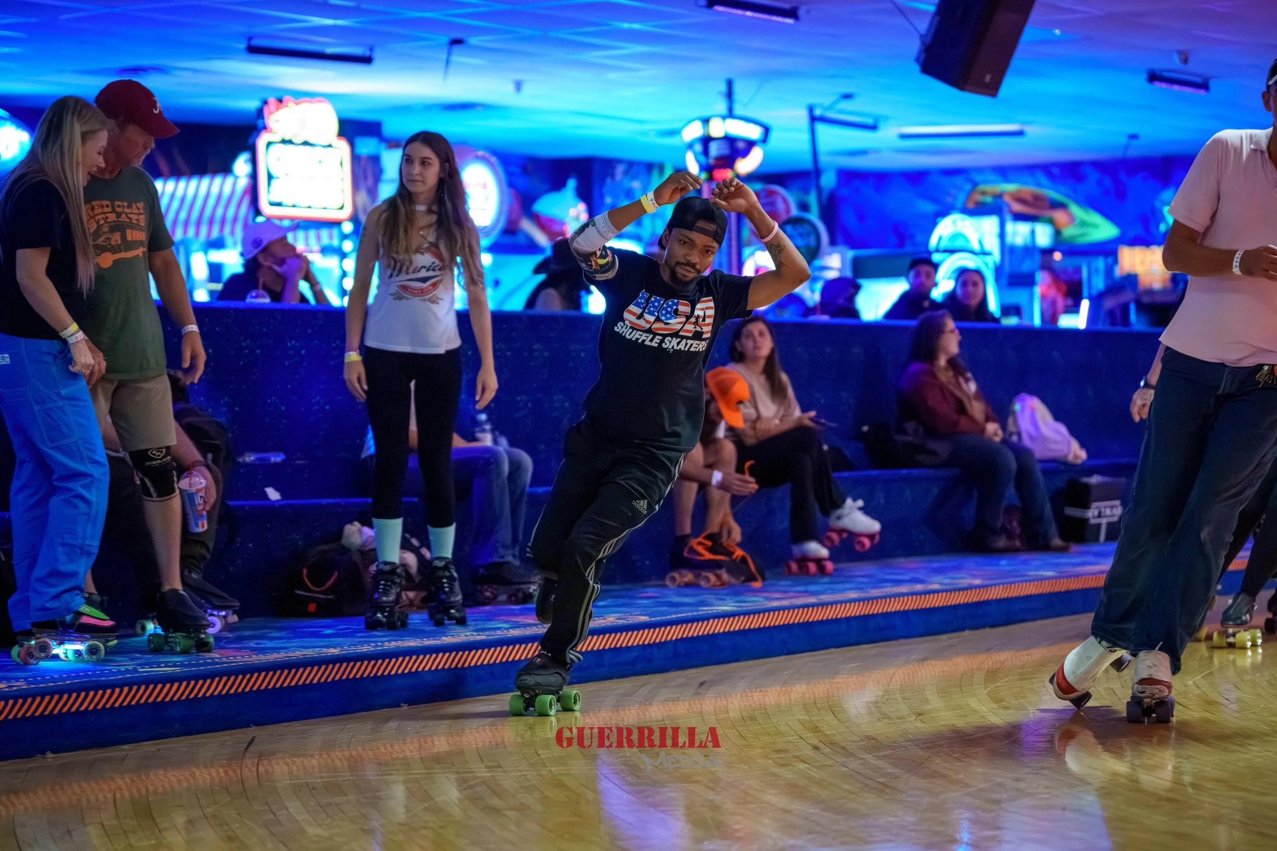 People roller skating in an indoor rink with neon lights, some sitting on a bench, and a man mid-dance move.