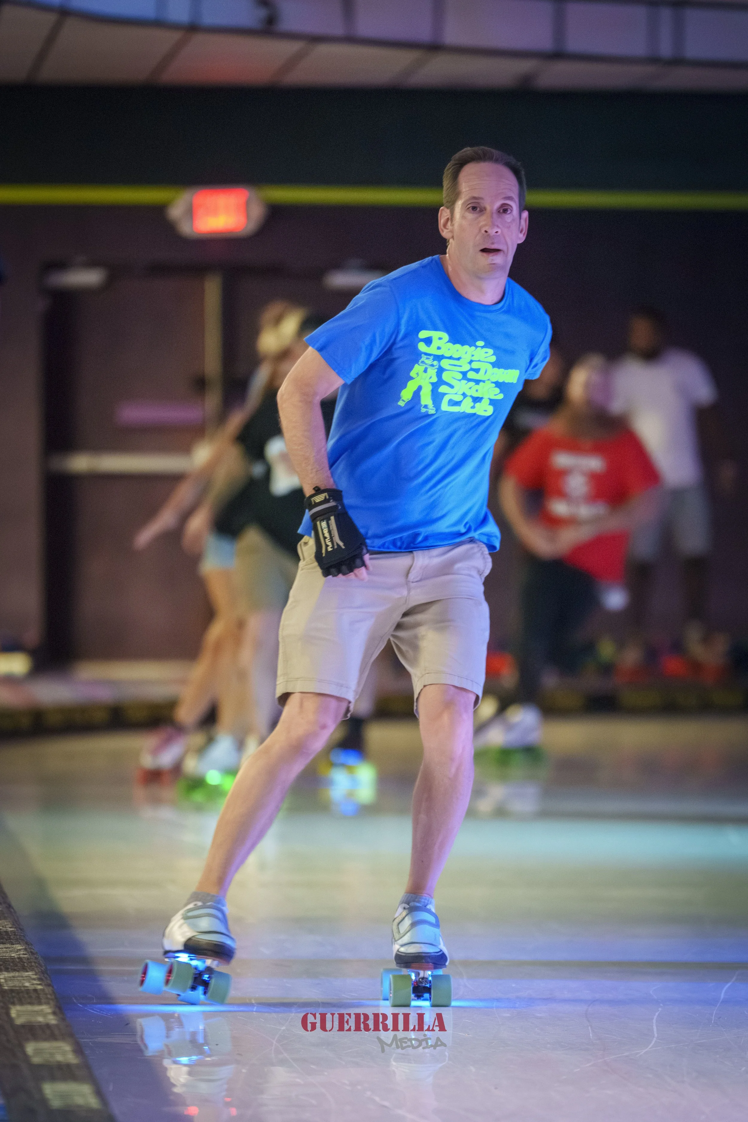A man roller skating in an indoor rink with other skaters in the background.