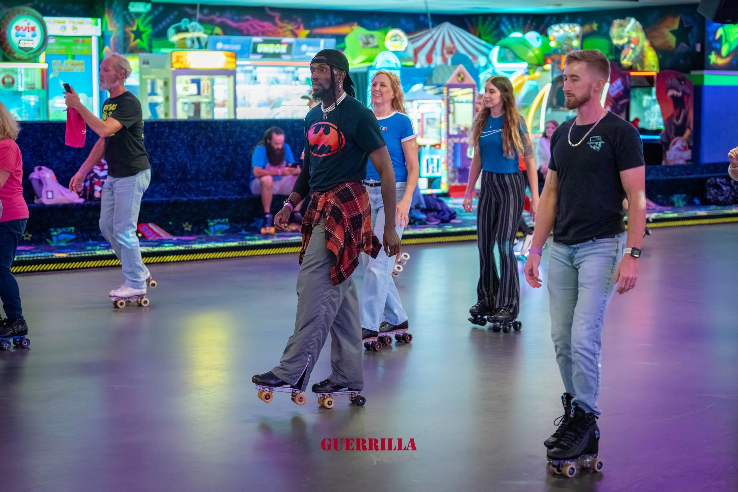 People roller skating in an arcade with colorful neon lights and game machines in the background.