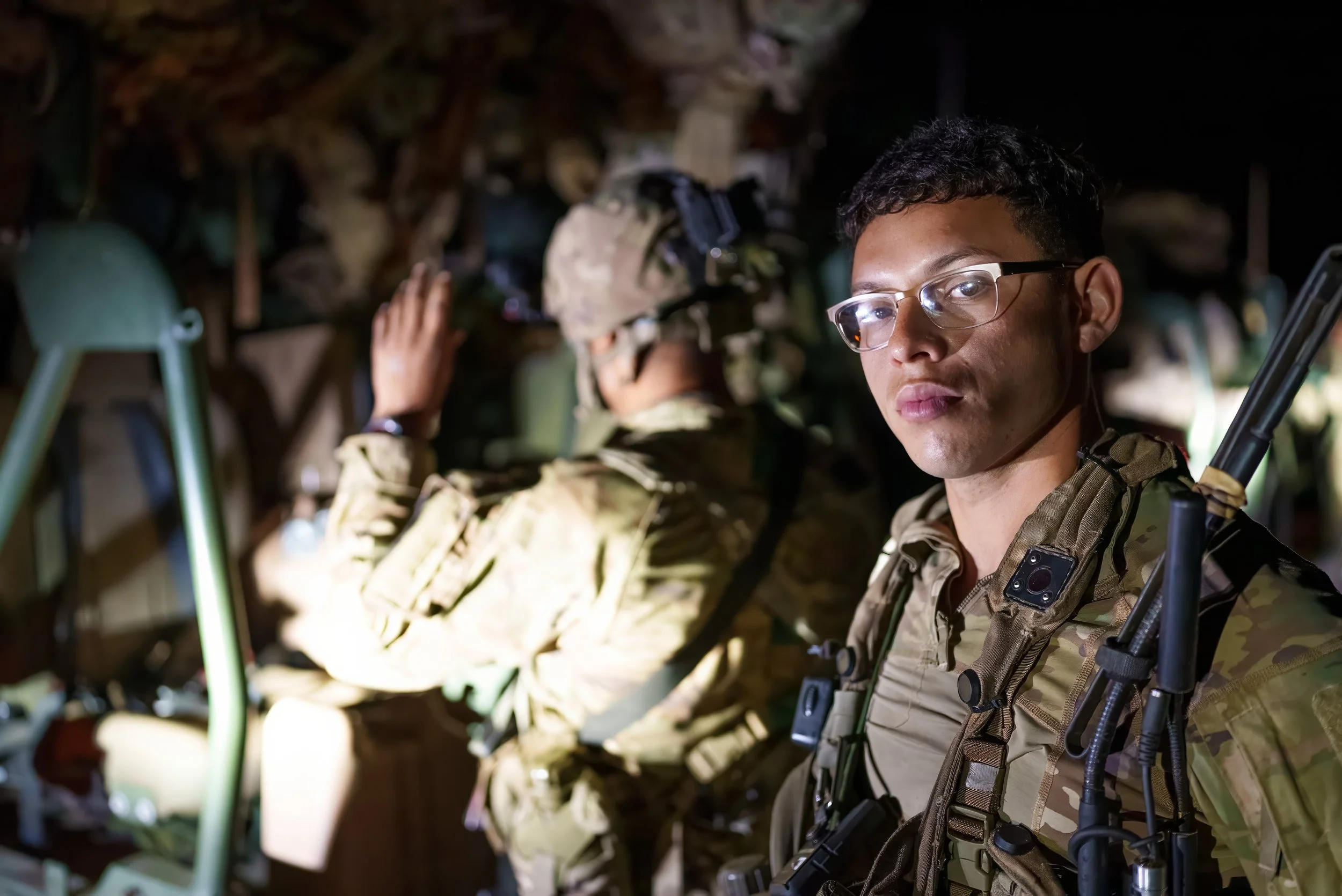 Two soldiers in camouflage uniforms inside a dimly lit military aircraft.