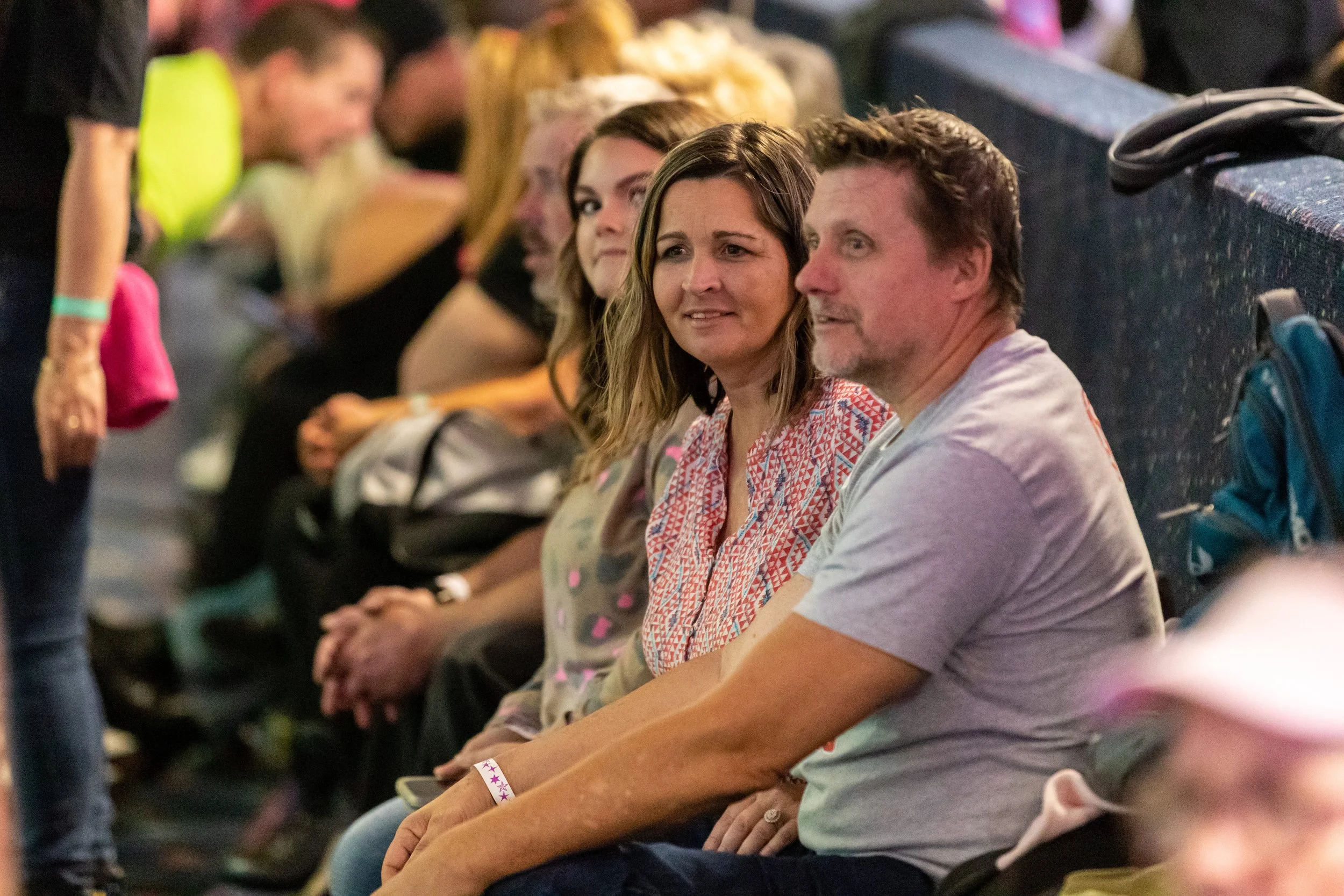 People sitting in a row at an event, with one woman and one man in focus, both looking towards the camera.