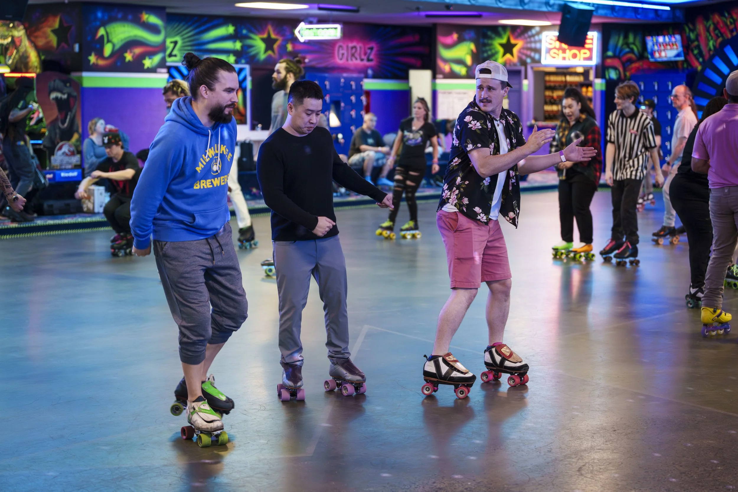 People roller skating at an indoor skate rink with colorful neon lights and graffiti-style decorations.