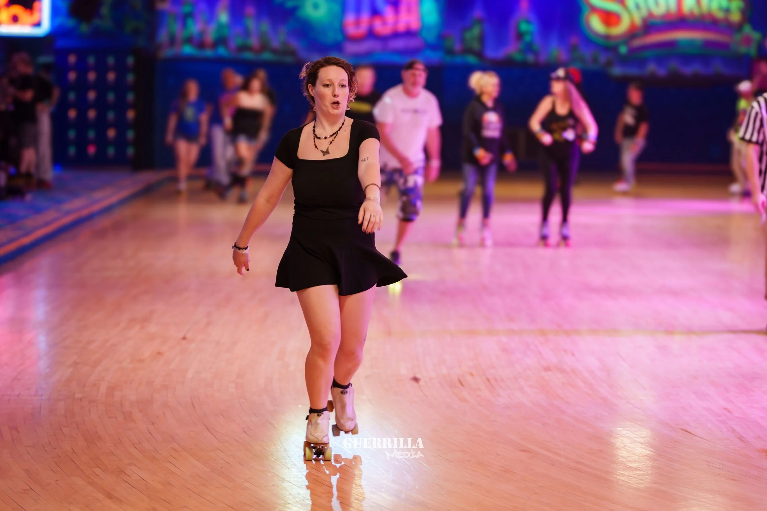 A woman roller skating in a roller rink, with other people in the background, under colorful neon lights.